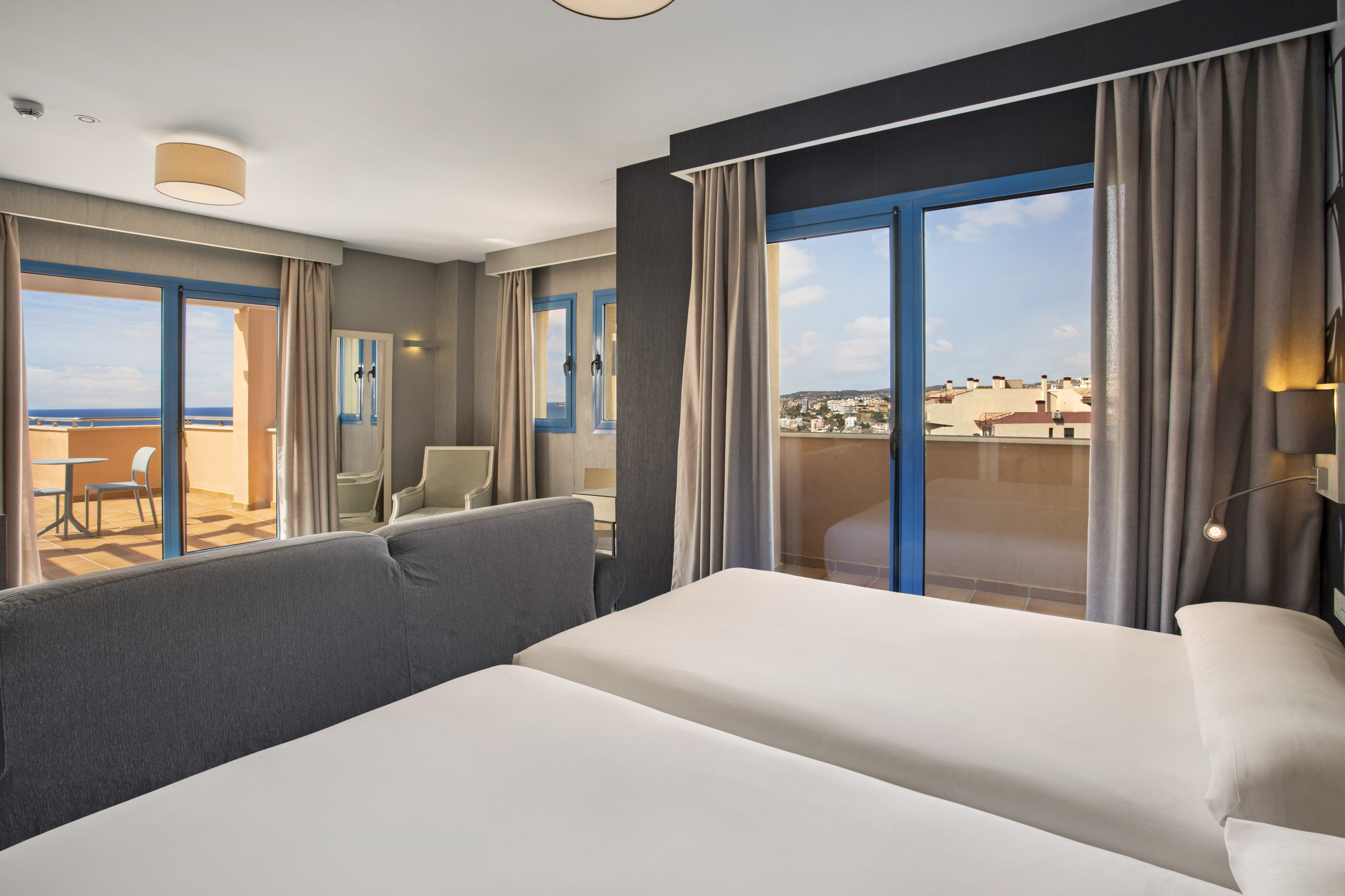 Modern hotel room with twin beds, two balconies showing ocean and city views.