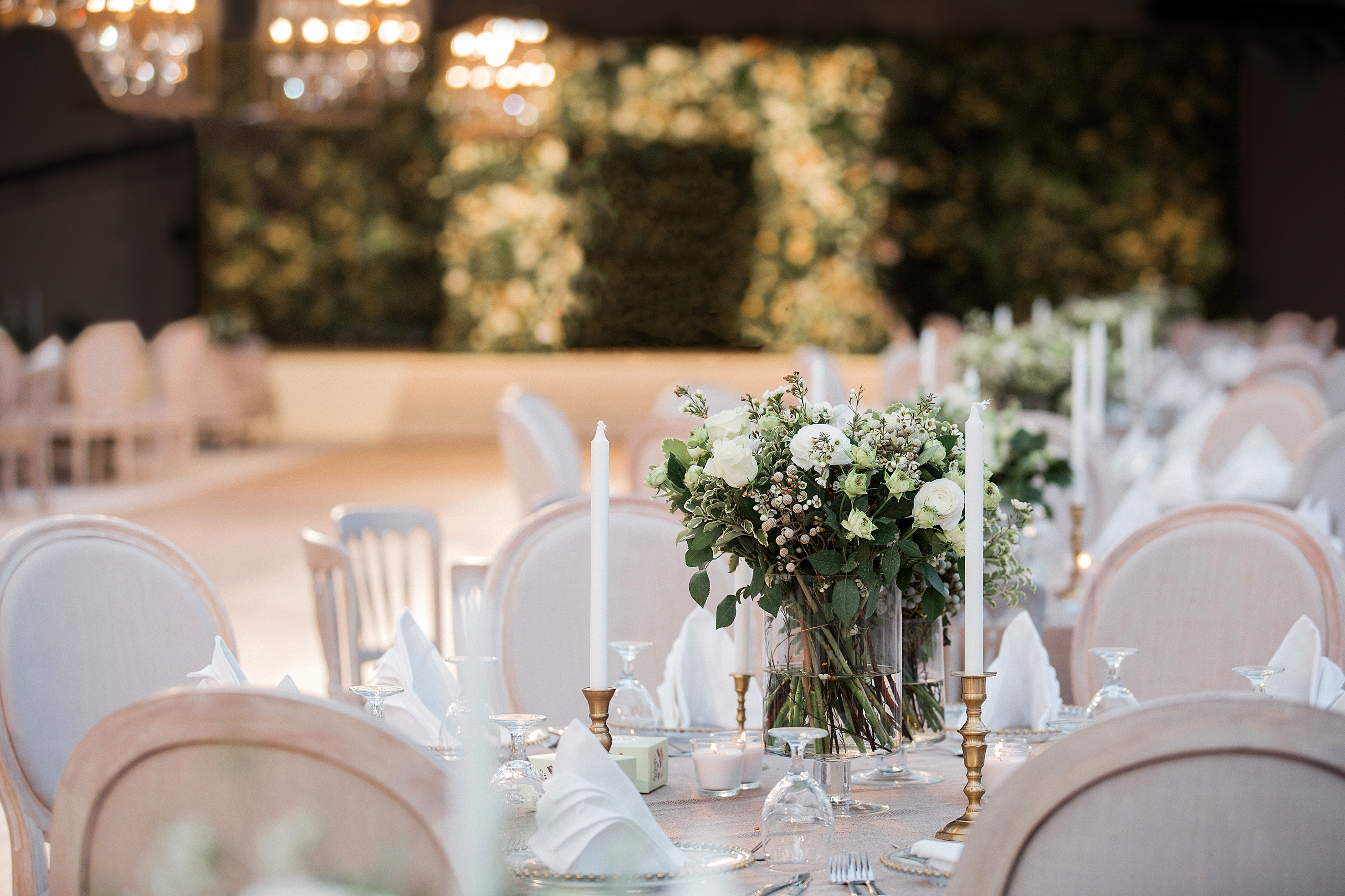 Elegant wedding table decor with white roses, greenery, and candles.