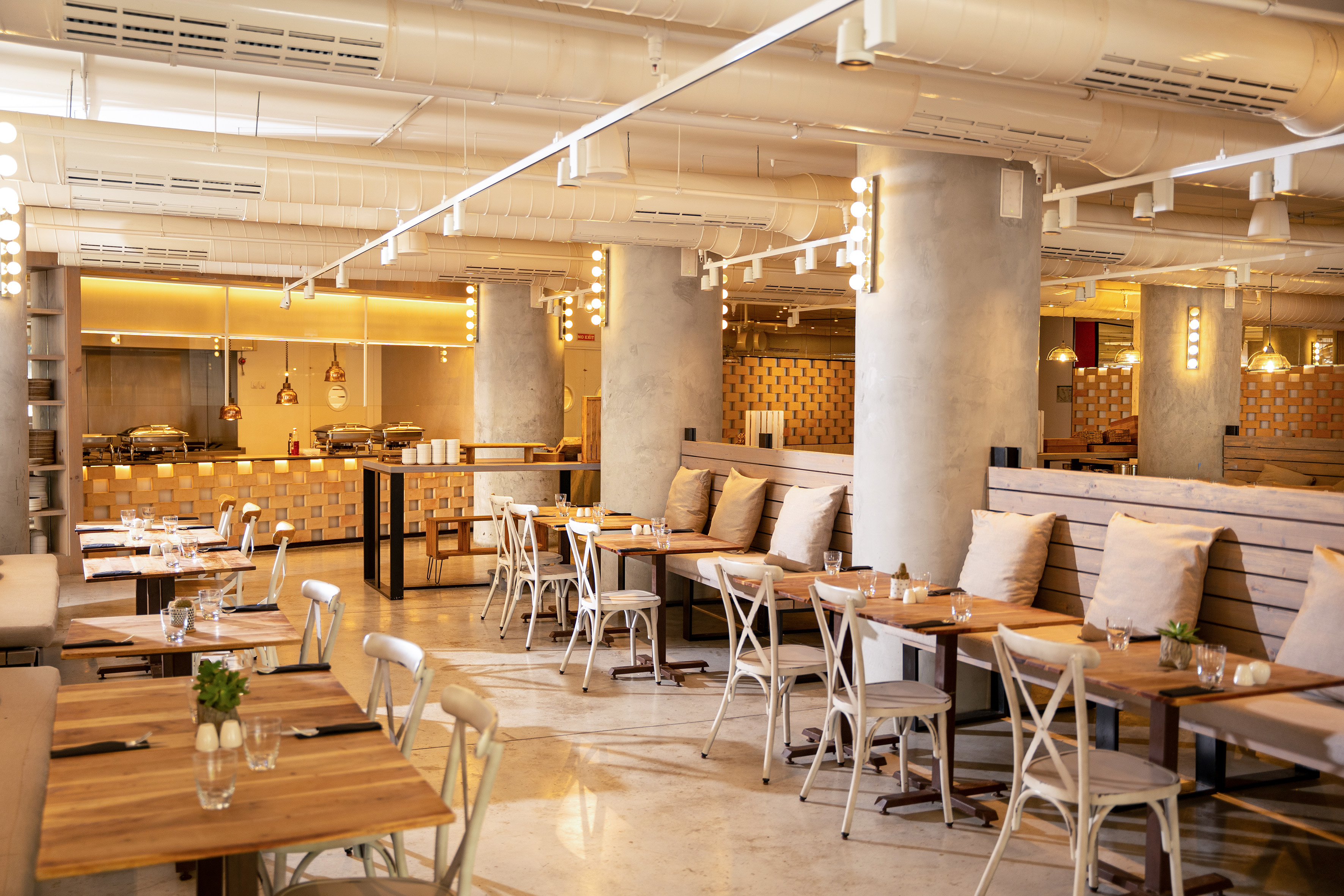 Modern restaurant dining room with wooden tables, white chairs, and buffet station.