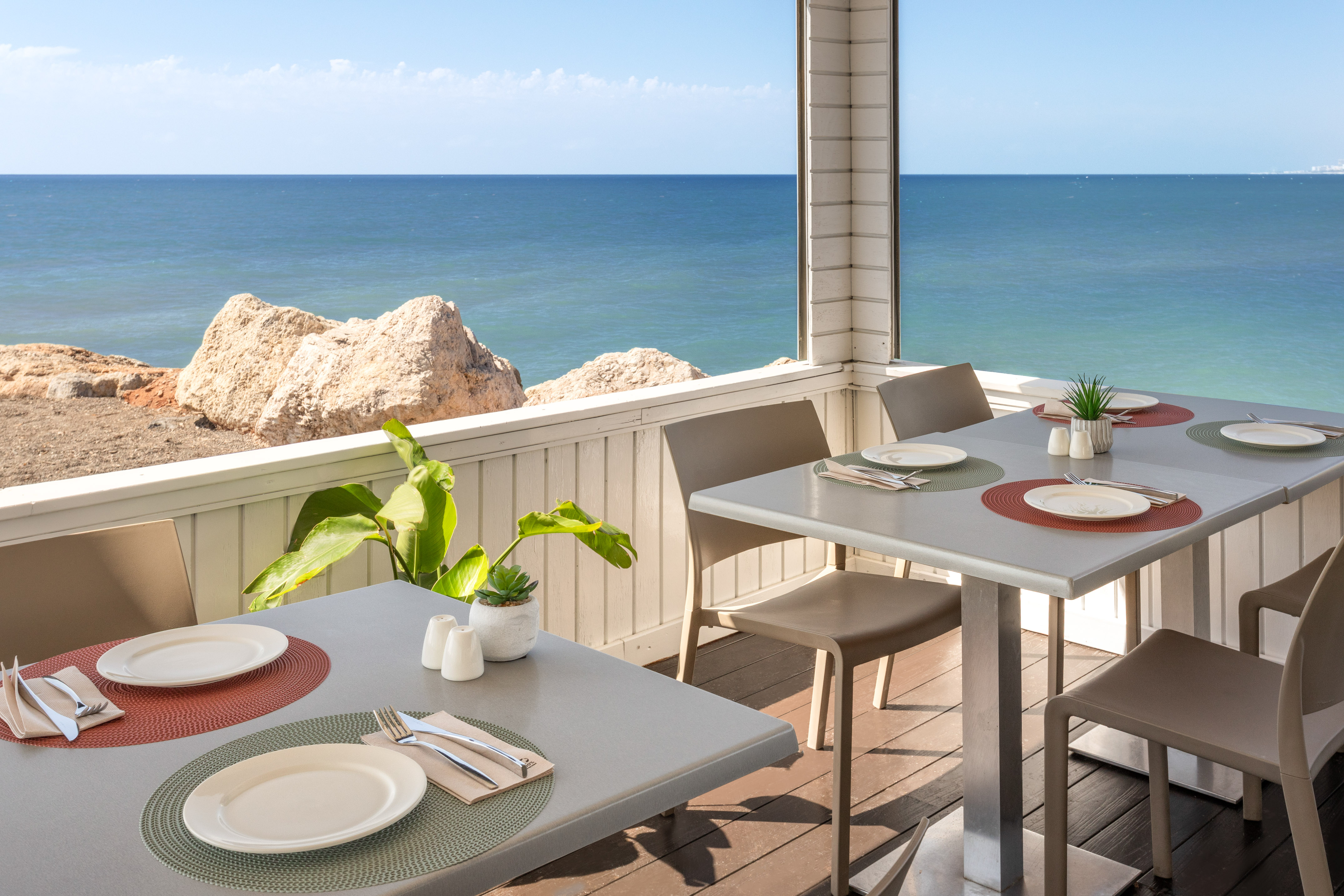 Terraza restaurante con mesas y vistas al mar y rocas en la costa.