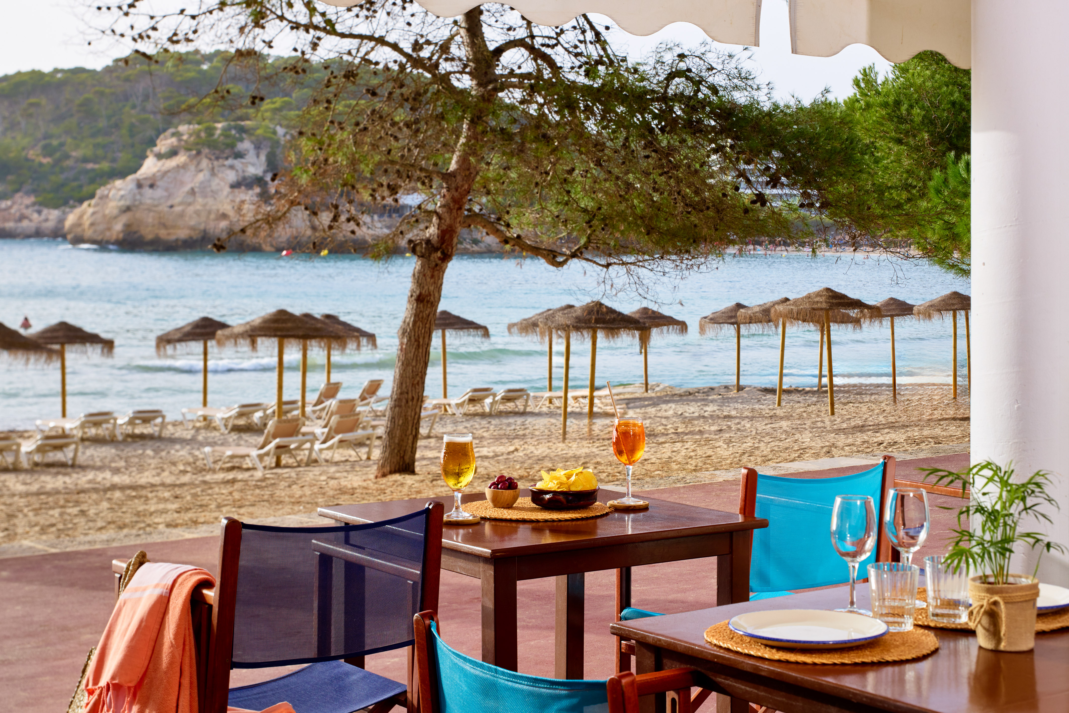 Beach bar with cocktails, snacks, sandy beach, straw umbrellas, and blue ocean.