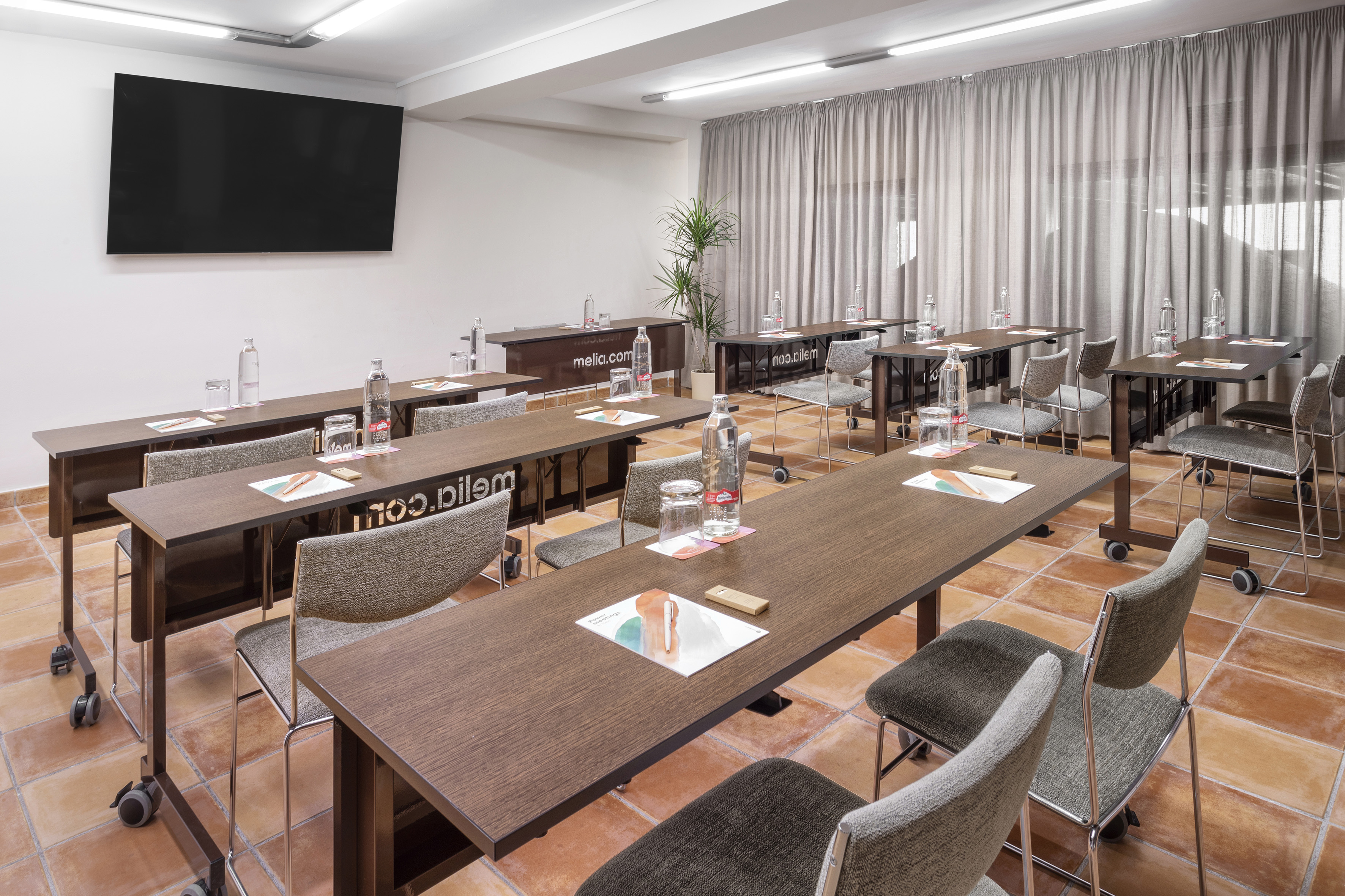 Meliá meeting room with tables, chairs, large screen, and water bottles.