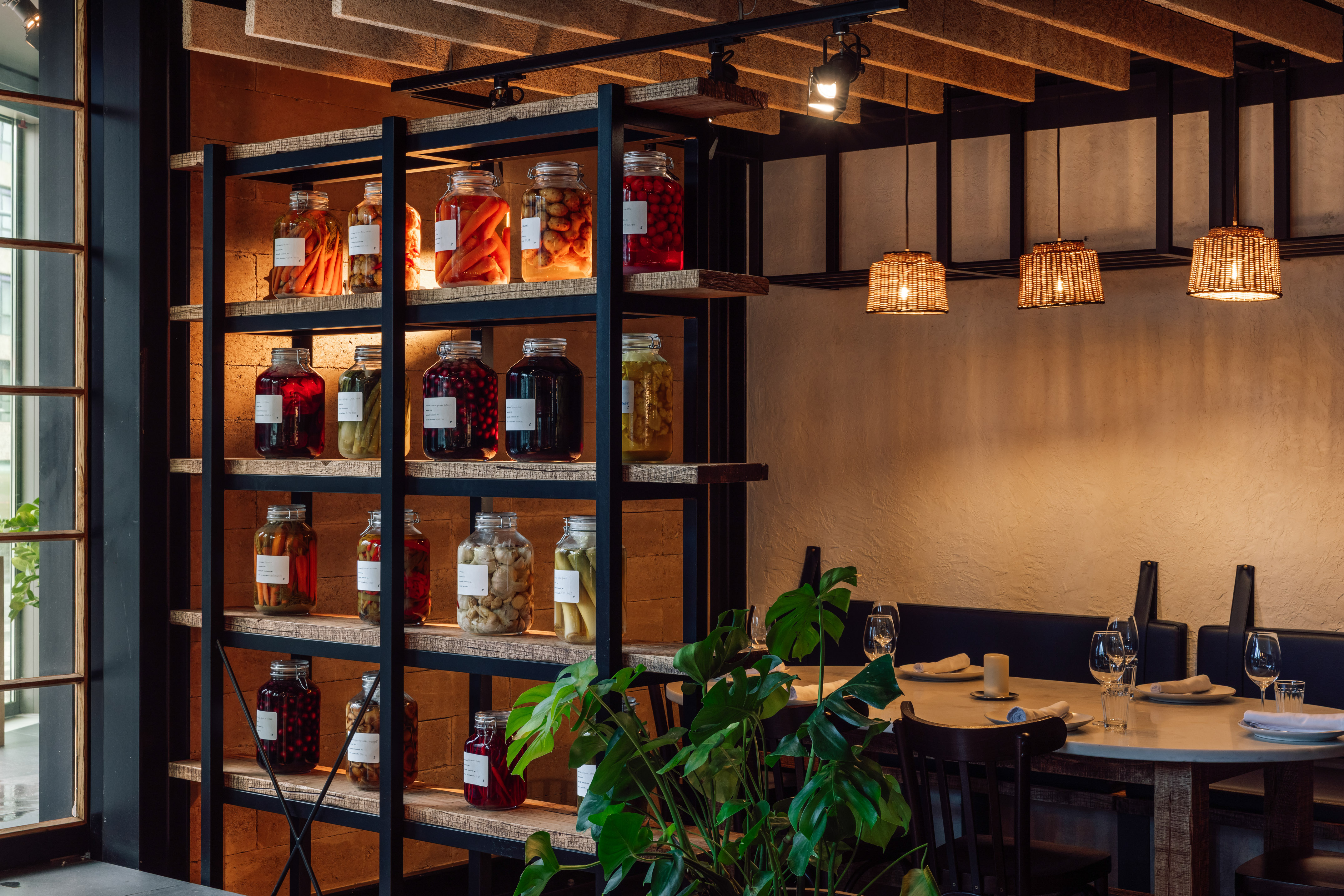 Modern rustic restaurant dining area with shelves of colorful pickled jars.
