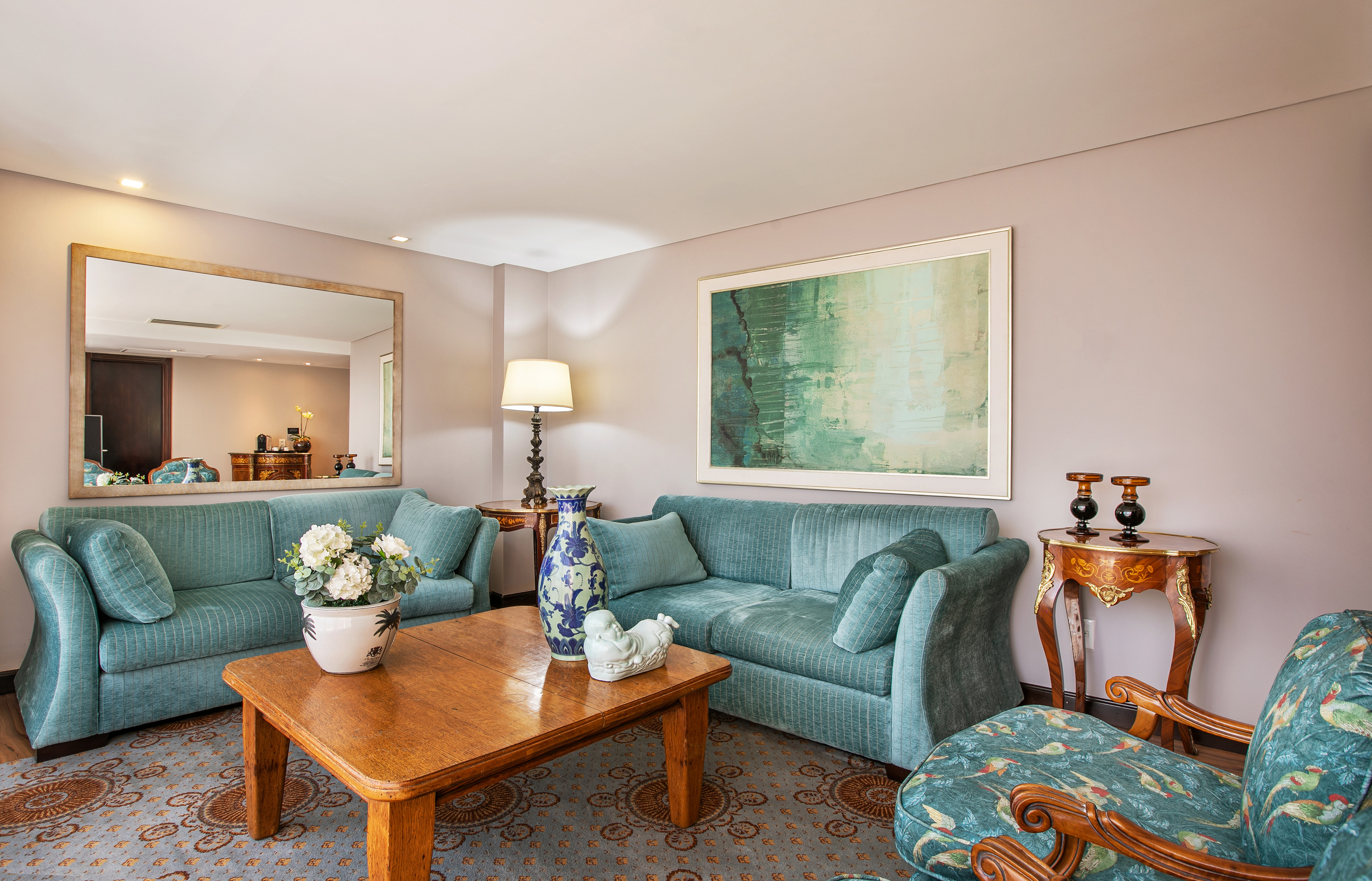 Teal sofas, wood coffee table, abstract art in a traditional living room with mirror.