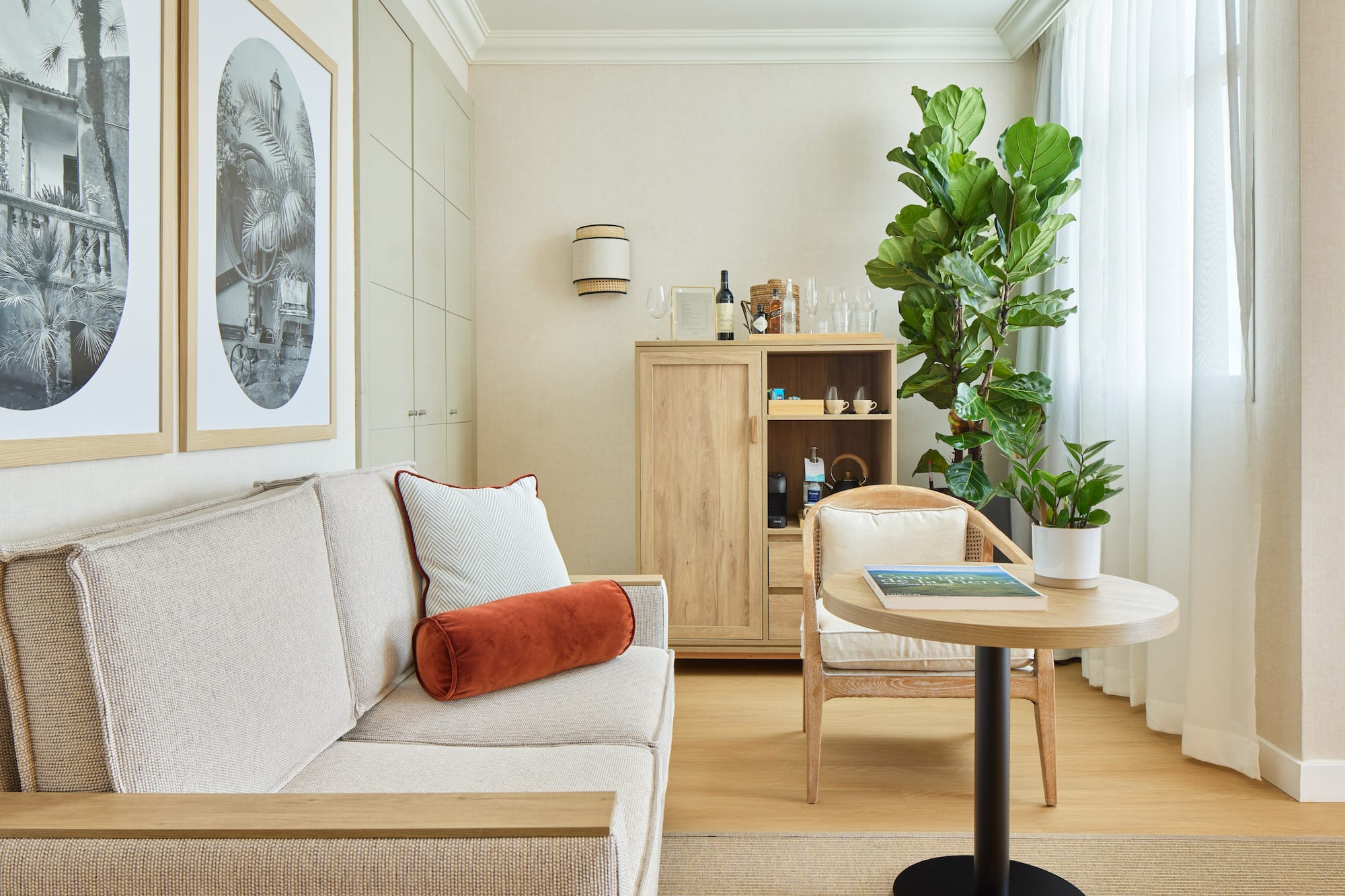 Neutral hotel suite with sofa, wooden cabinet, plants, and framed art.