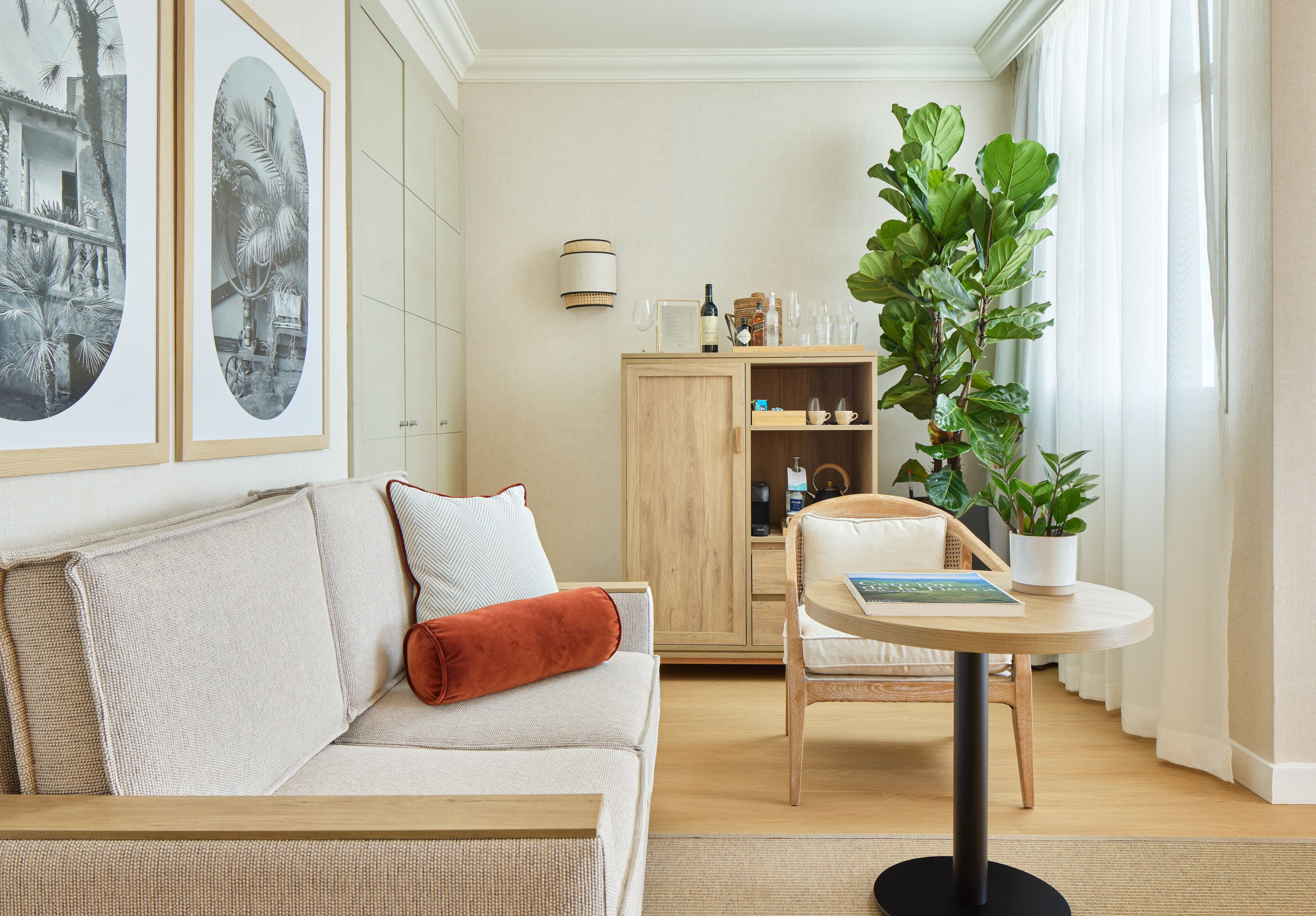 Neutral hotel suite with sofa, wooden cabinet, plants, and framed art.