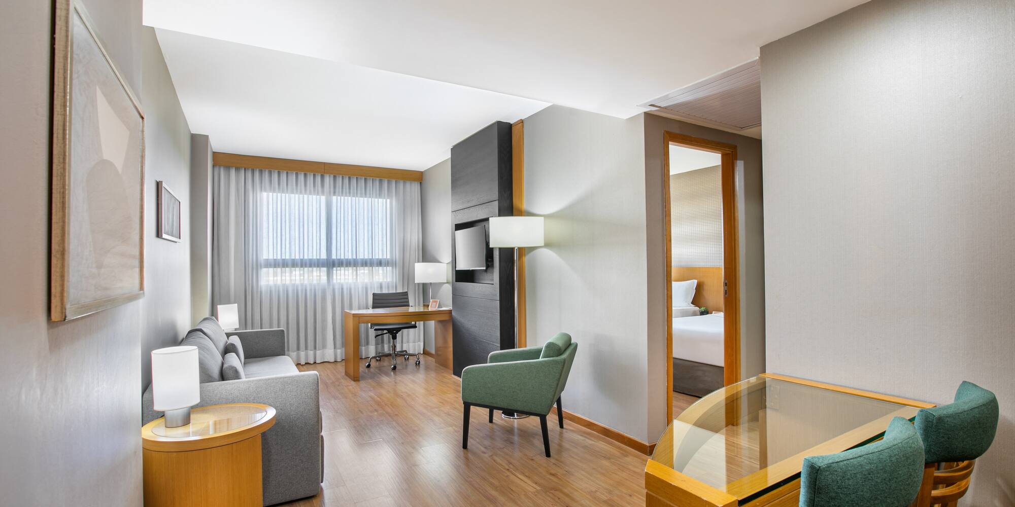 Modern hotel suite living room with sofa, desk, and connecting bedroom.