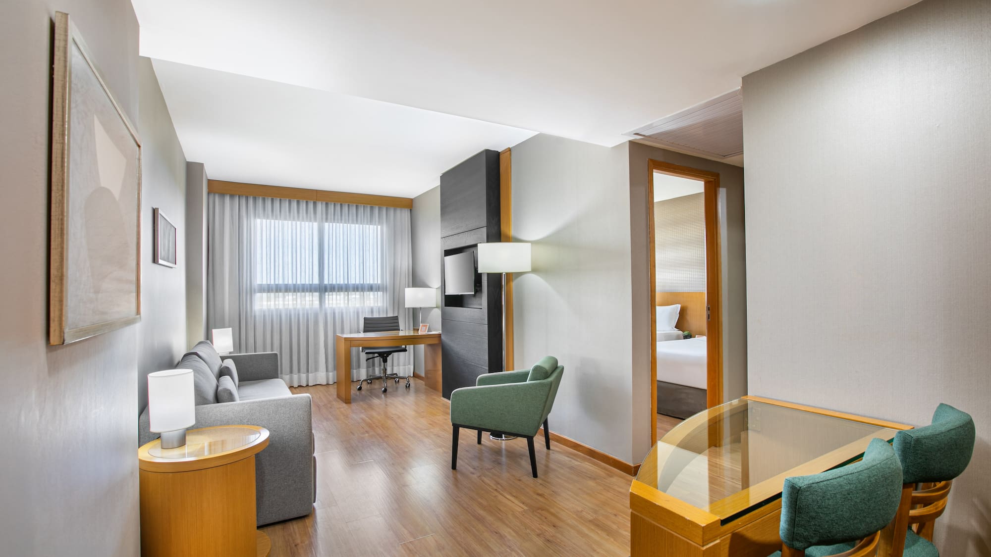 Modern hotel suite living room with sofa, desk, and connecting bedroom.