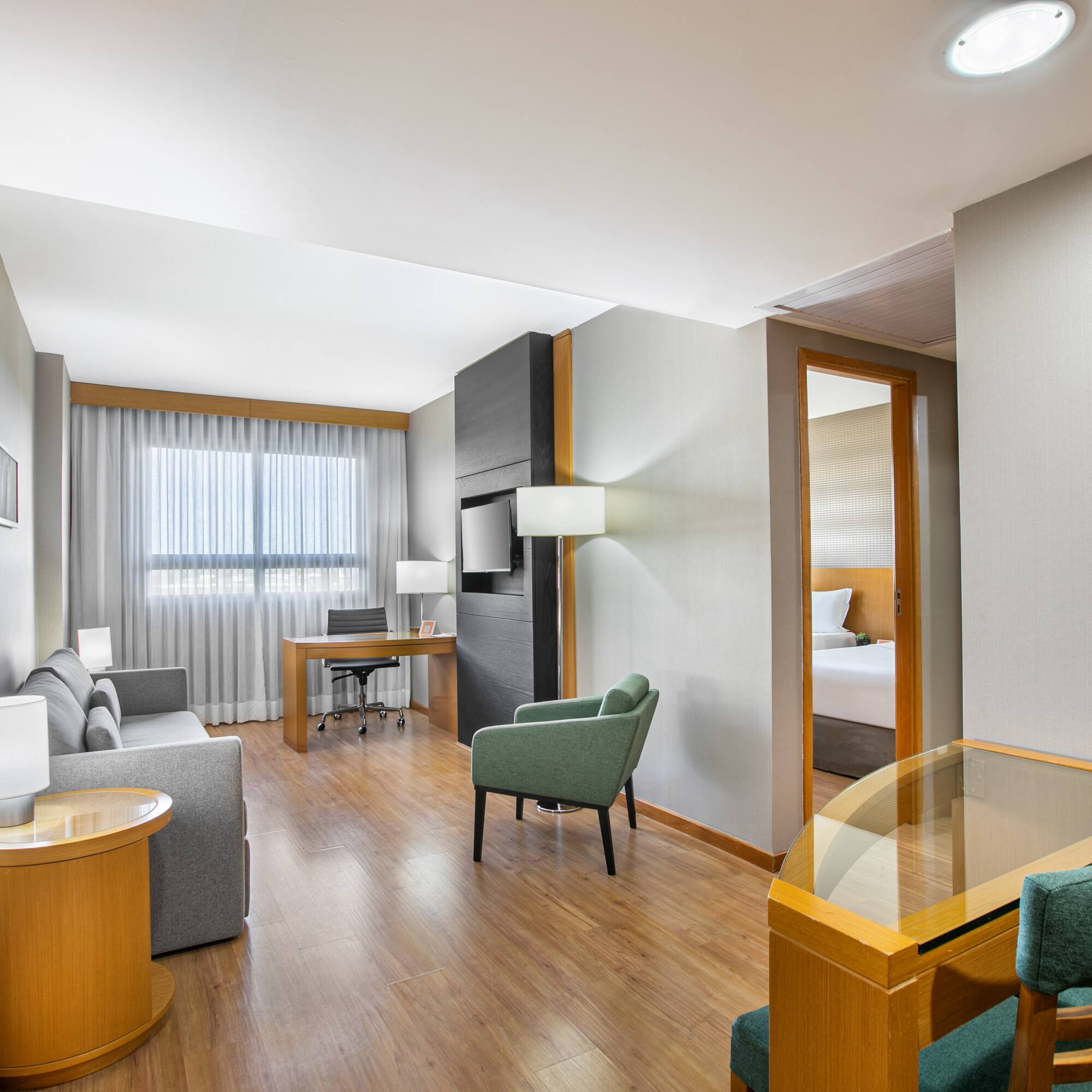 Modern hotel suite living room with sofa, desk, and connecting bedroom.