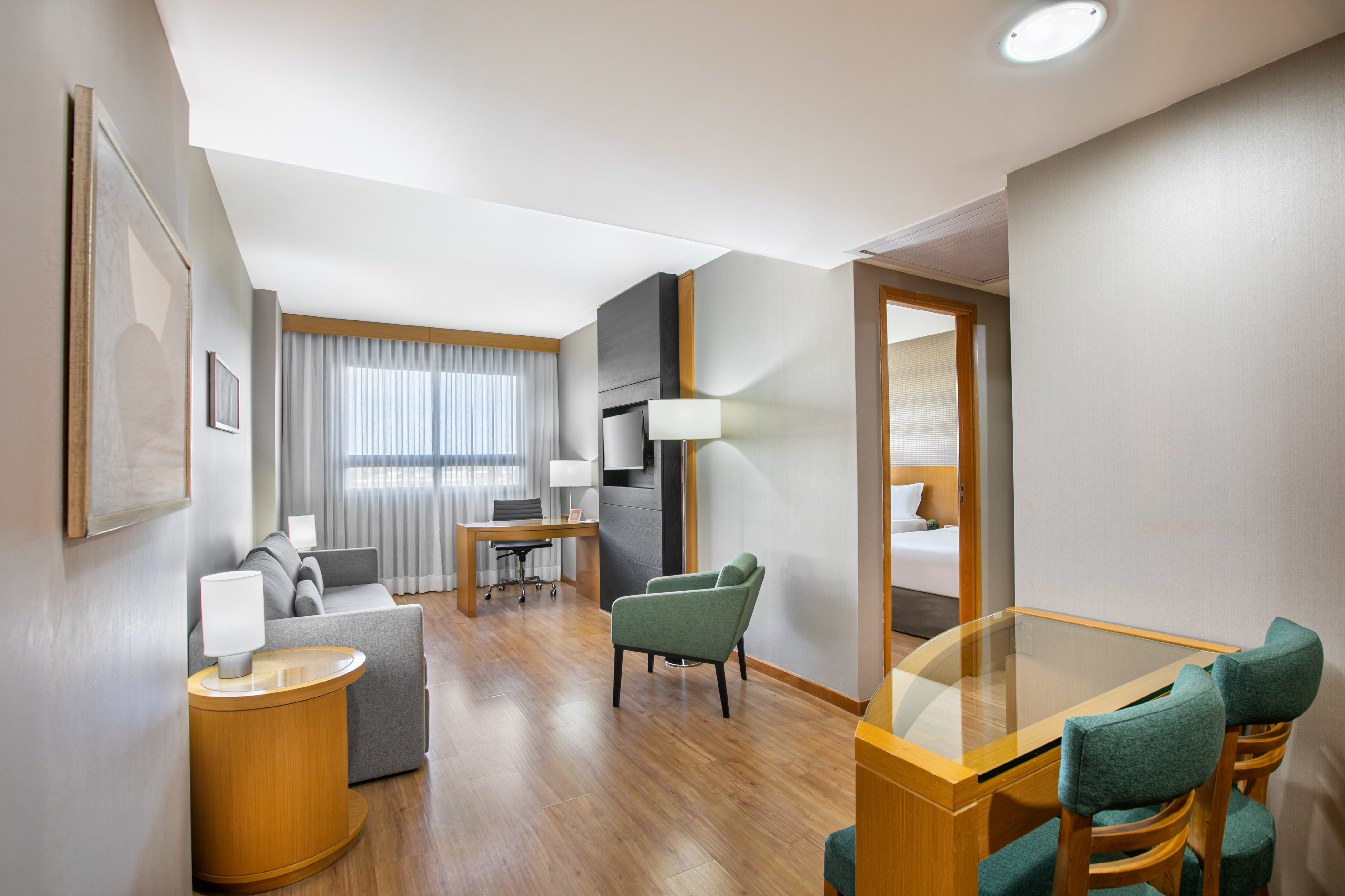Modern hotel suite living room with sofa, desk, and connecting bedroom.