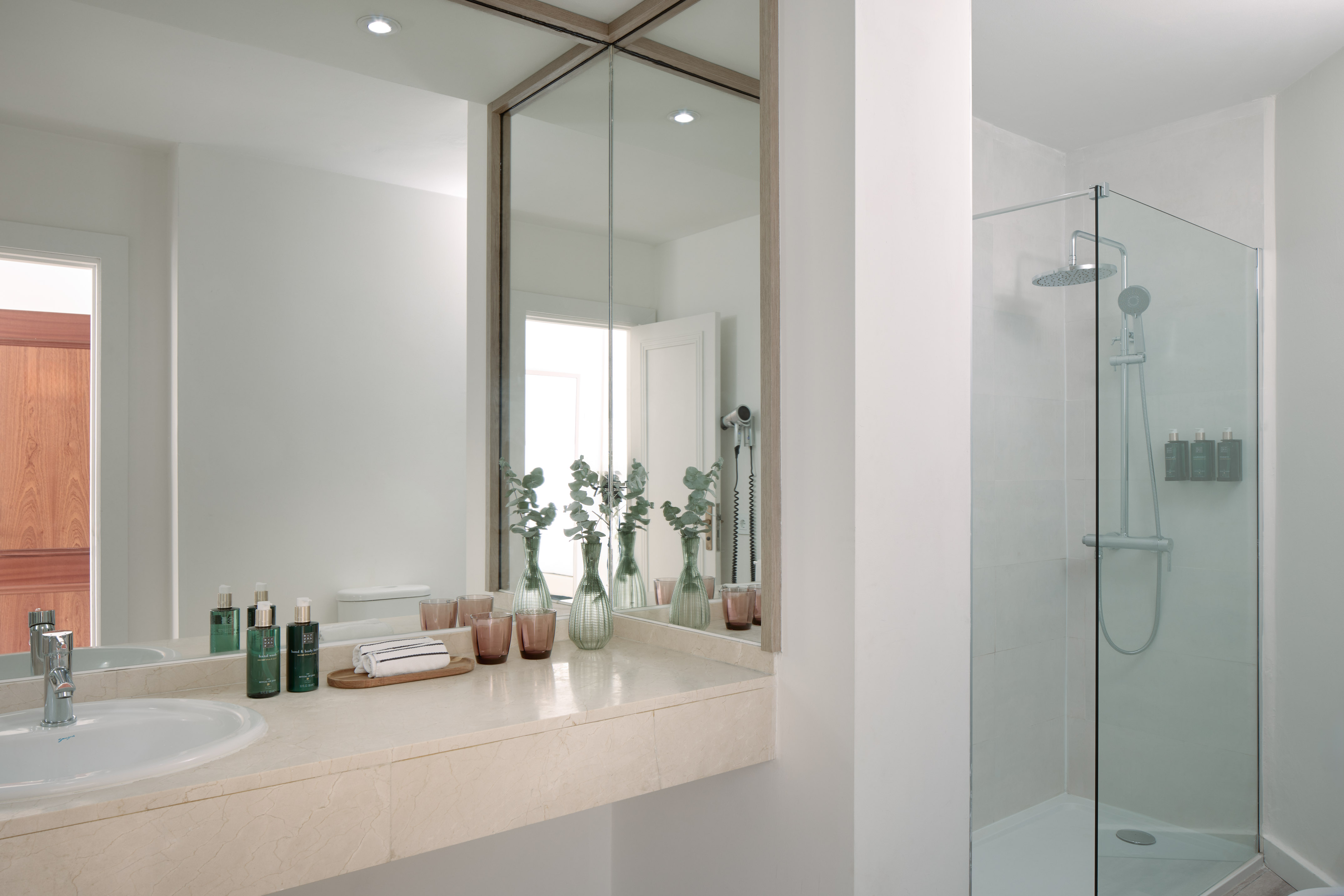 Modern hotel bathroom with marble vanity, mirror, and glass shower.