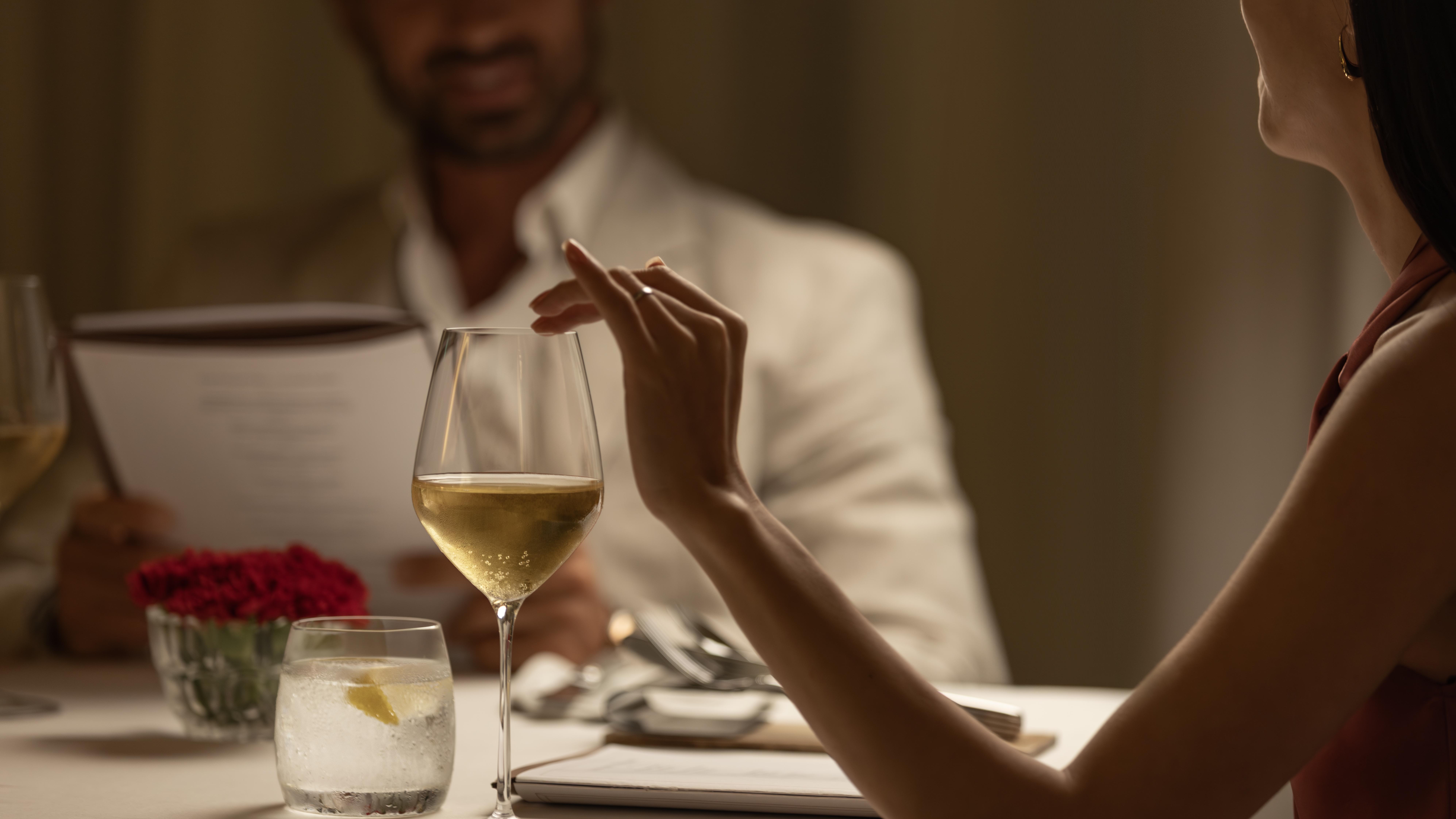 Couple dining, woman with sparkling wine, man reading restaurant menu.