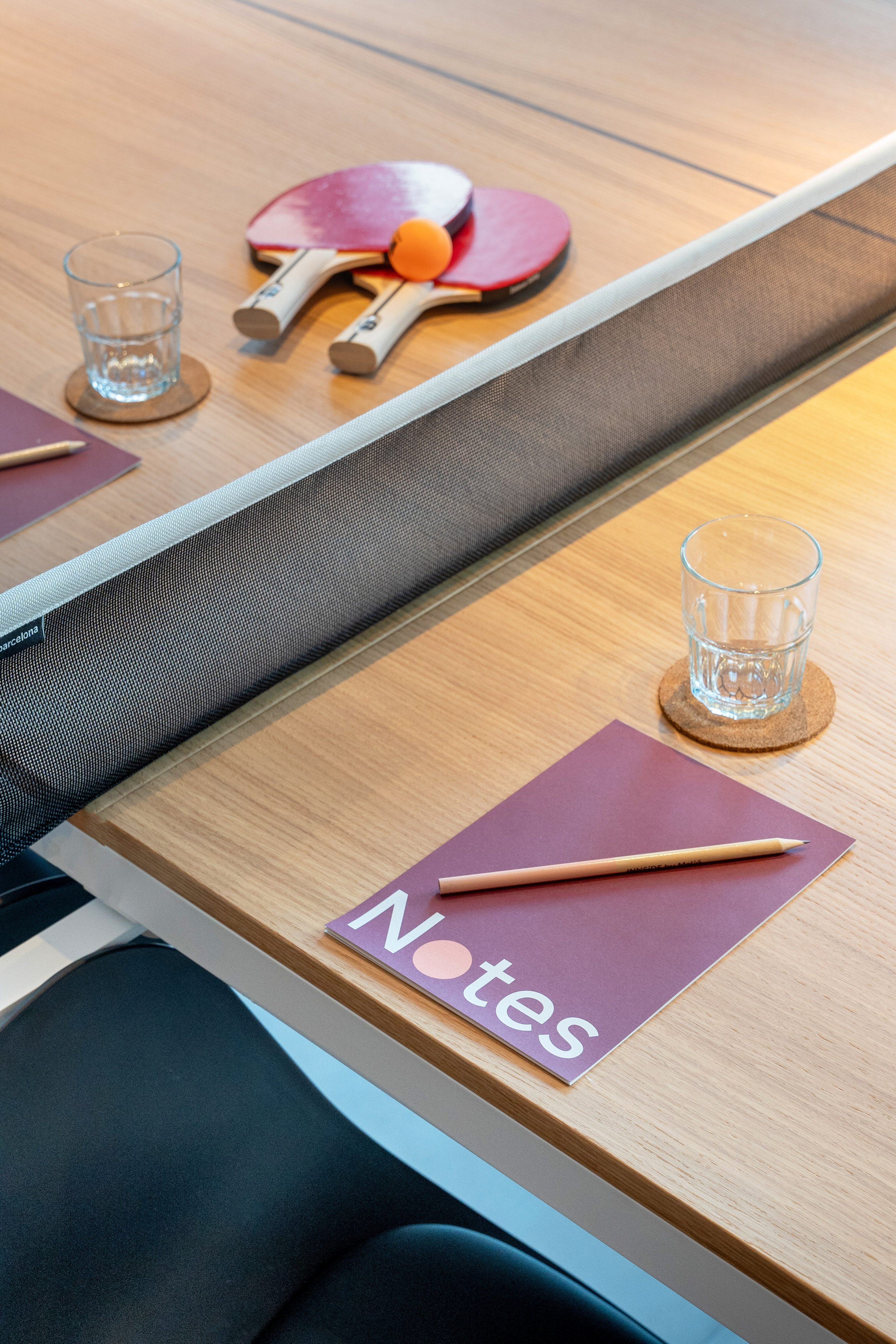 Modern office ping pong table with paddles, ball, notebook, and glasses.