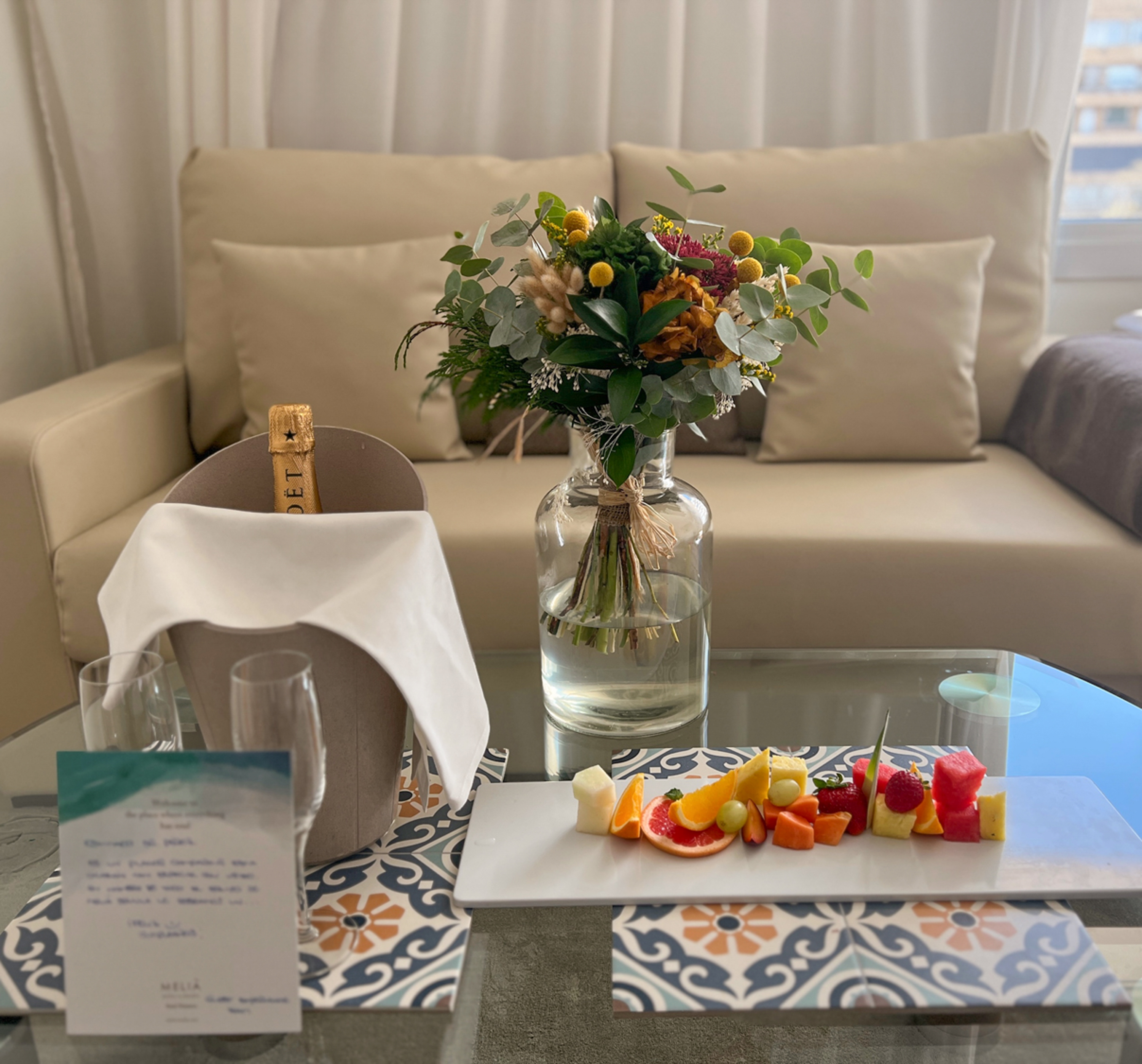 Champán, flores y fruta en mesa de cristal, detalle de bienvenida Meliá.