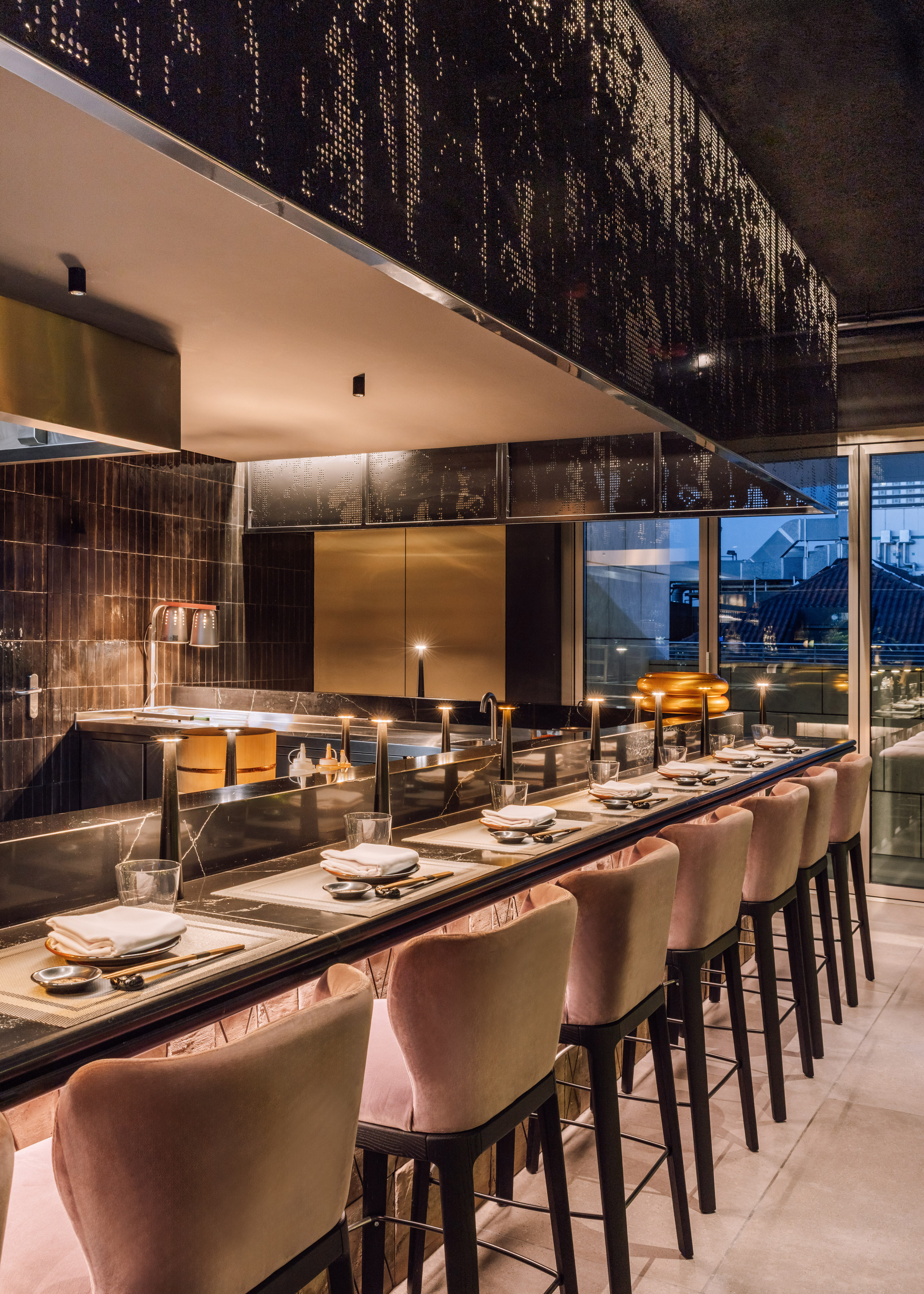 Modern upscale sushi bar with dark marble counter, pink stools, and ambient lighting.