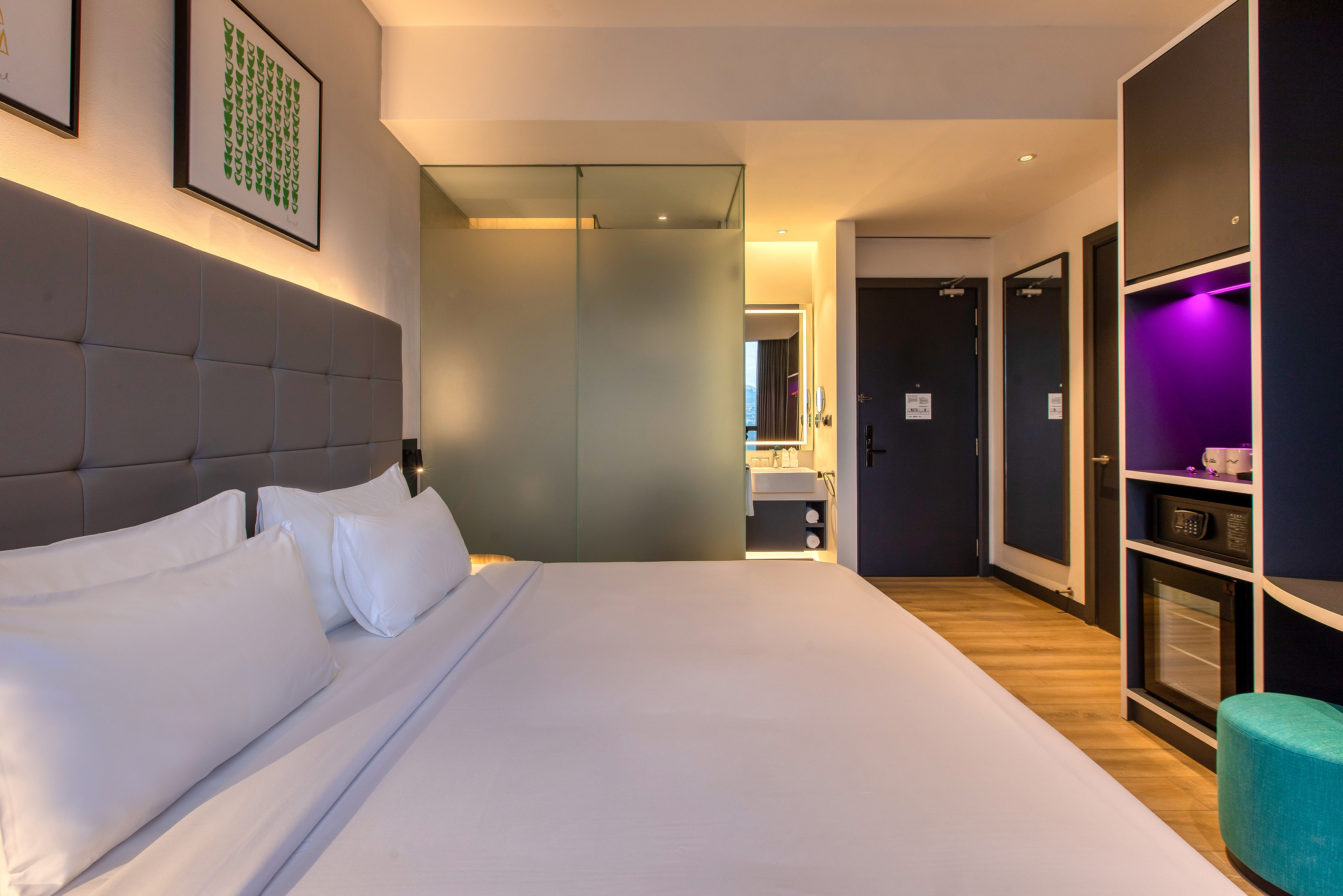 Modern hotel room with king bed, backlit headboard, and frosted glass bathroom.