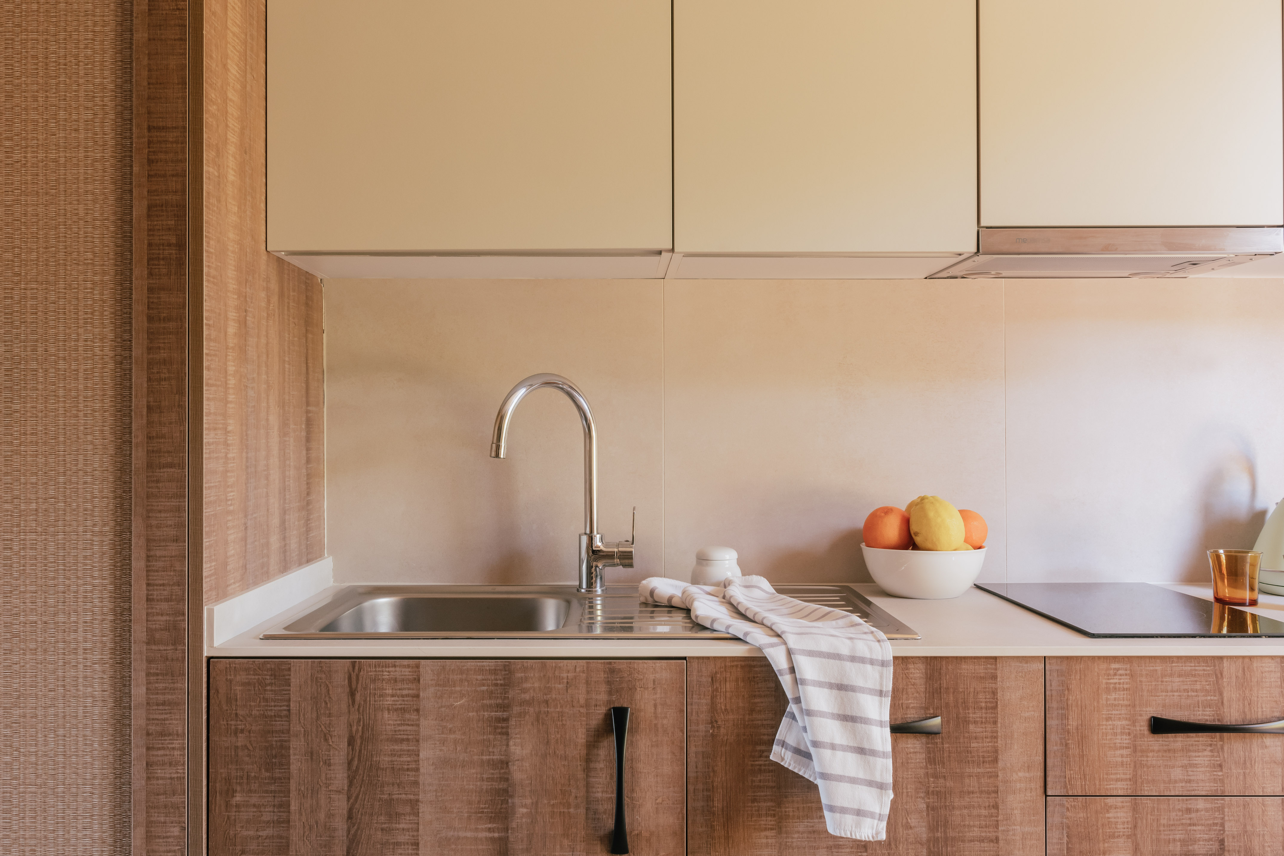 Modern kitchen with wood cabinets, steel sink, induction hob, and fruit.