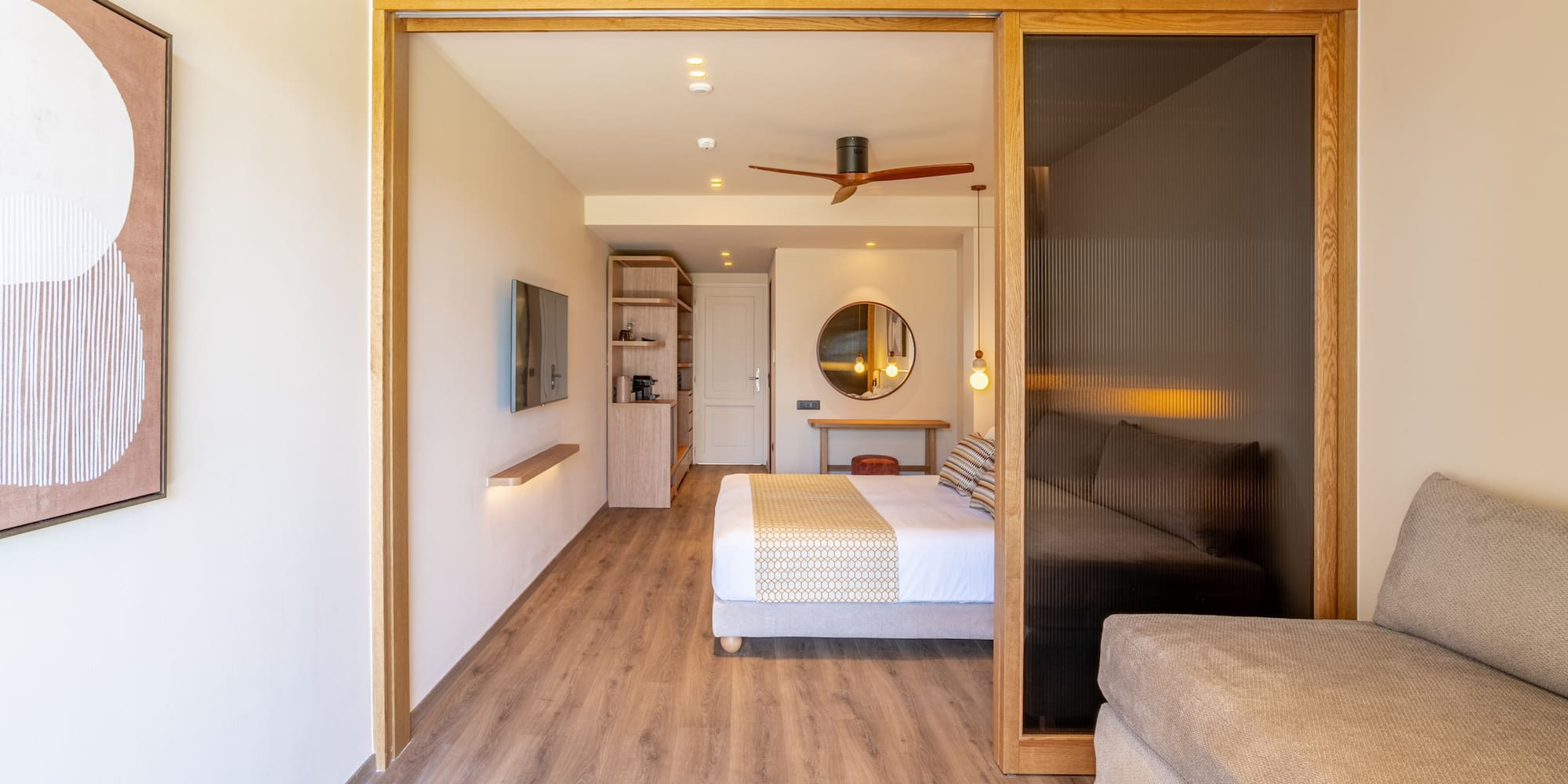 Modern hotel suite featuring bedroom, sofa, wood floors, and sliding doors.