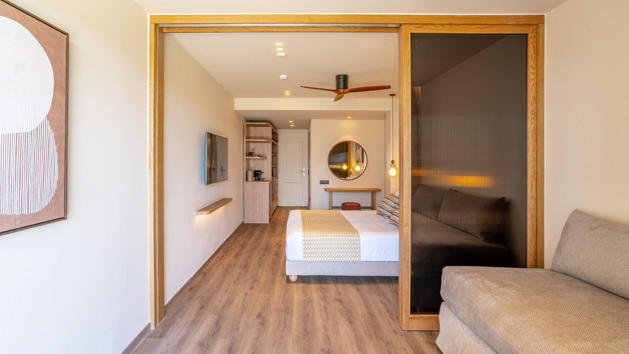 Modern hotel suite featuring bedroom, sofa, wood floors, and sliding doors.