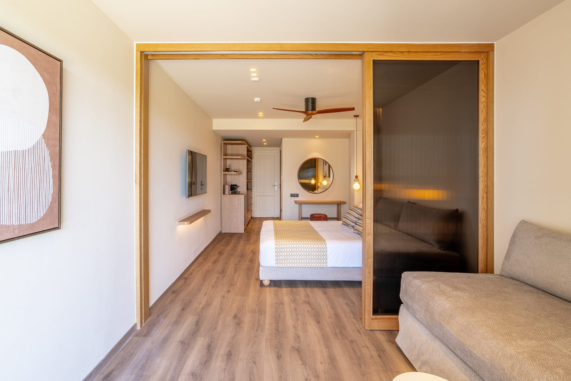 Modern hotel suite featuring bedroom, sofa, wood floors, and sliding doors.