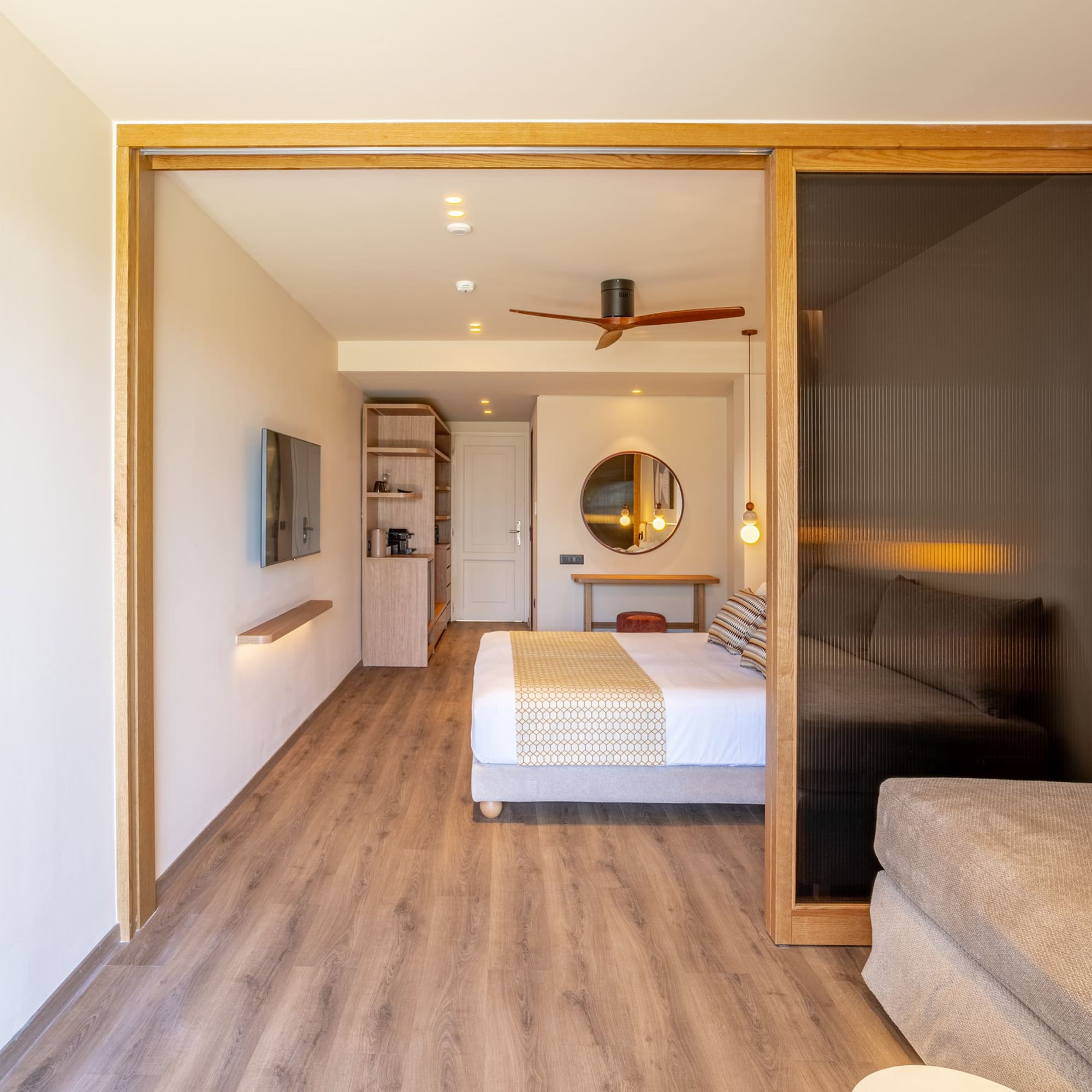 Modern hotel suite featuring bedroom, sofa, wood floors, and sliding doors.