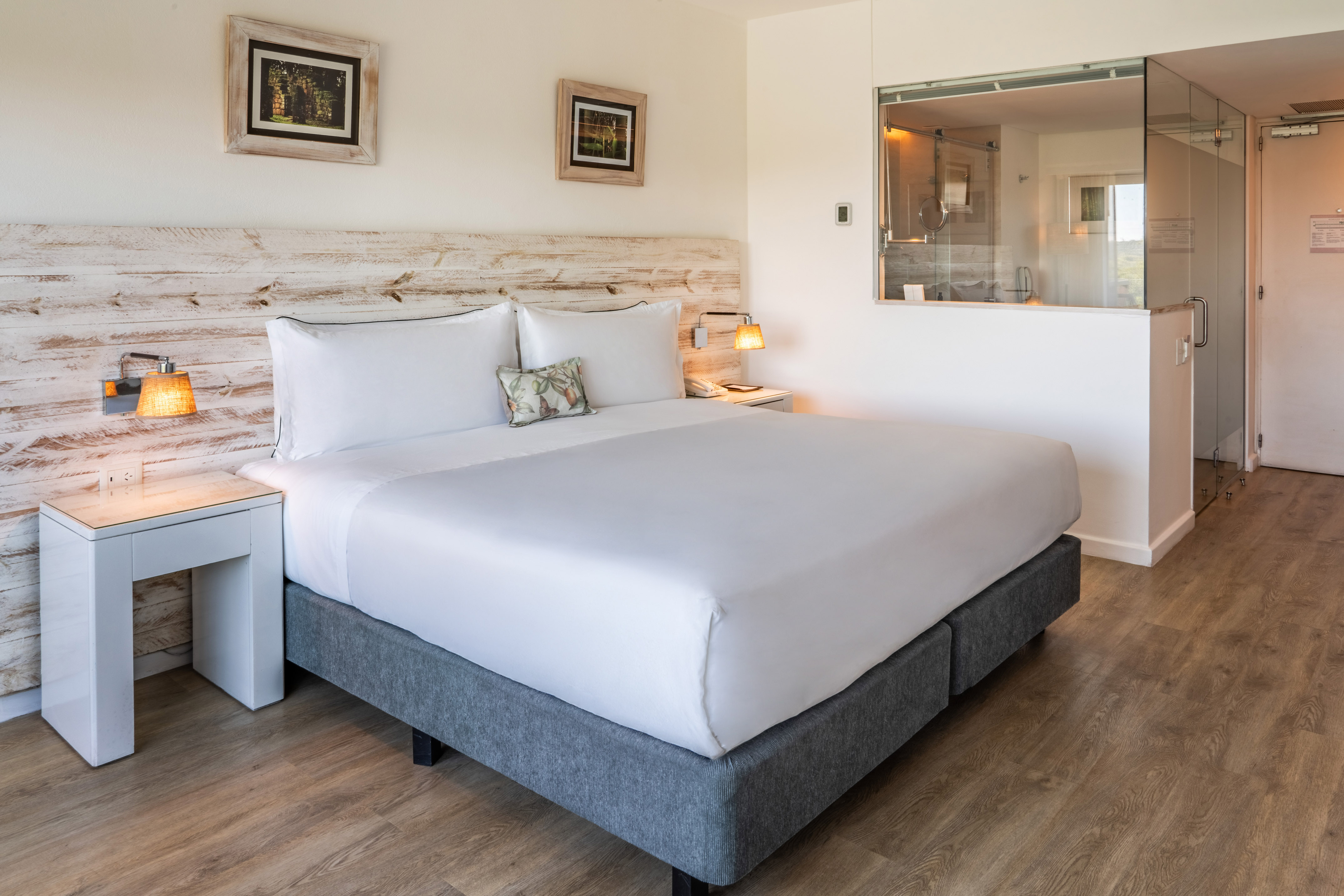 Modern hotel room with king bed, rustic headboard, and glass shower.