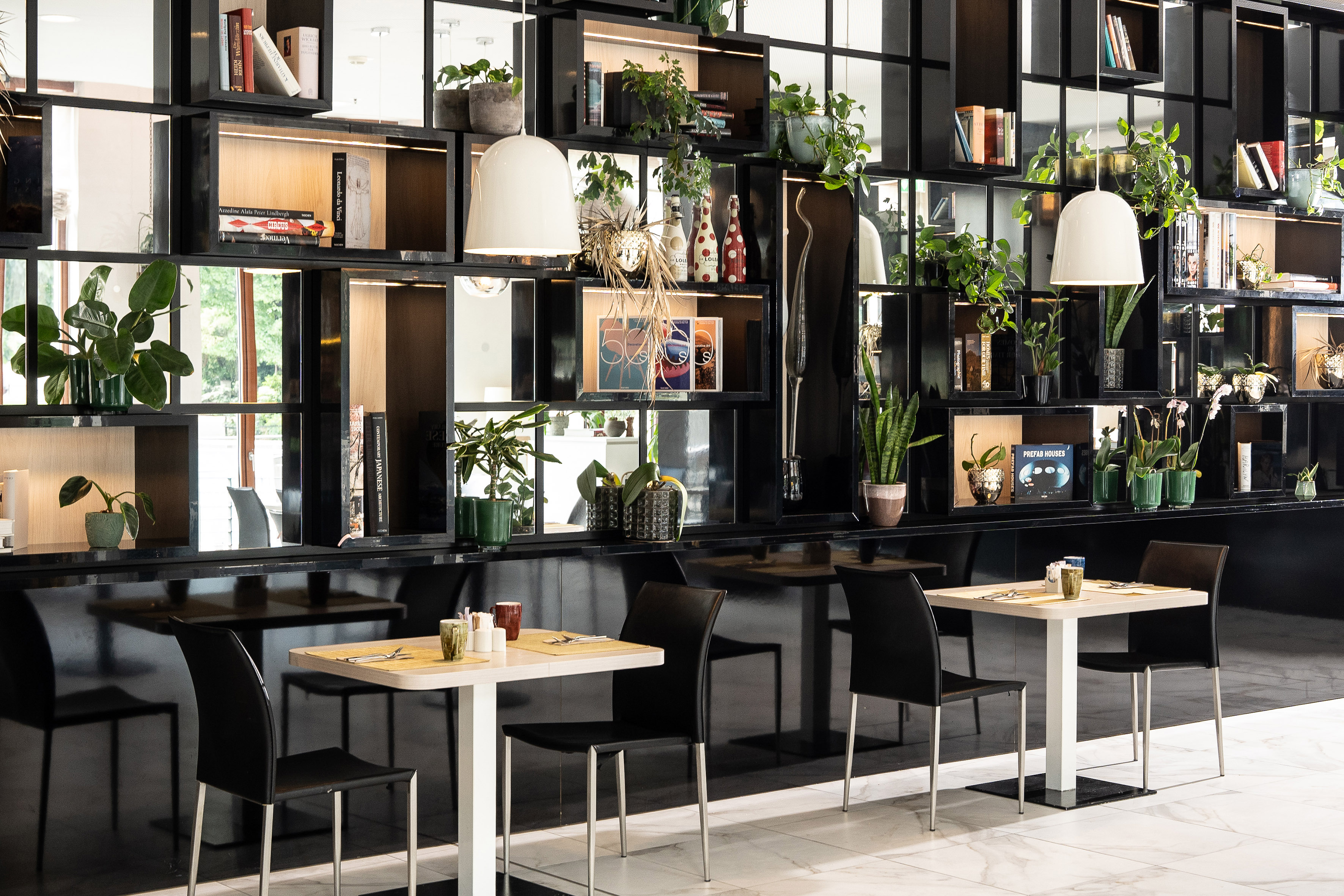 Modern restaurant interior with black shelves, plants, books, and dining tables.