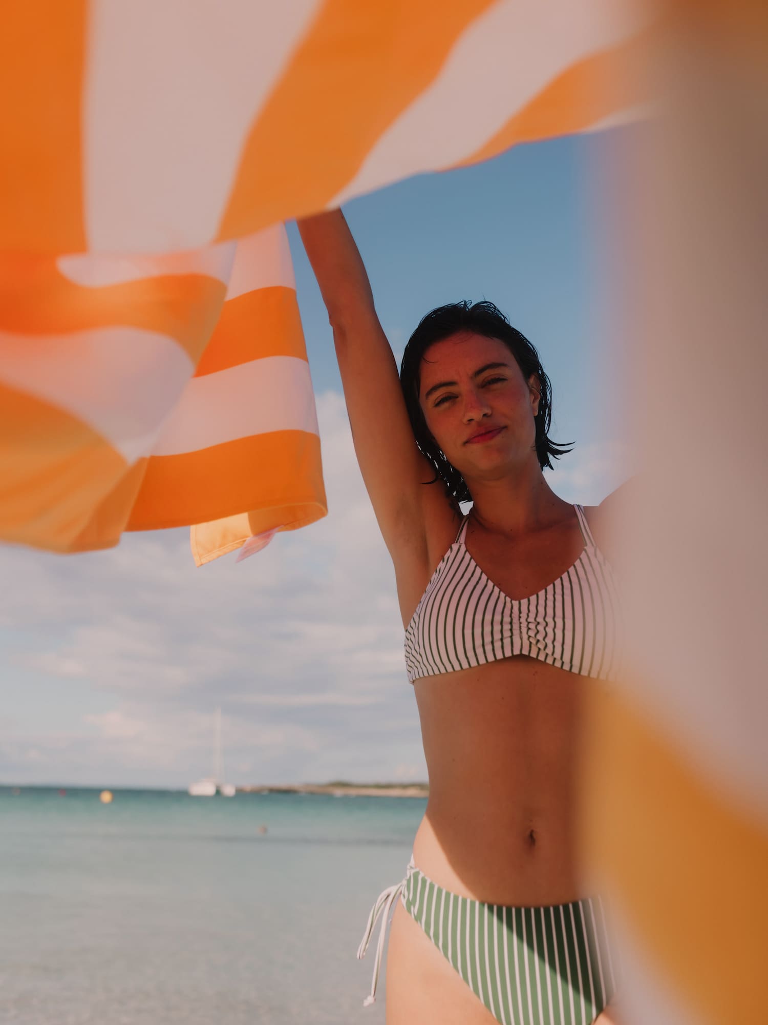 Woman in a bikini holding an orange and white striped towel at the beach.