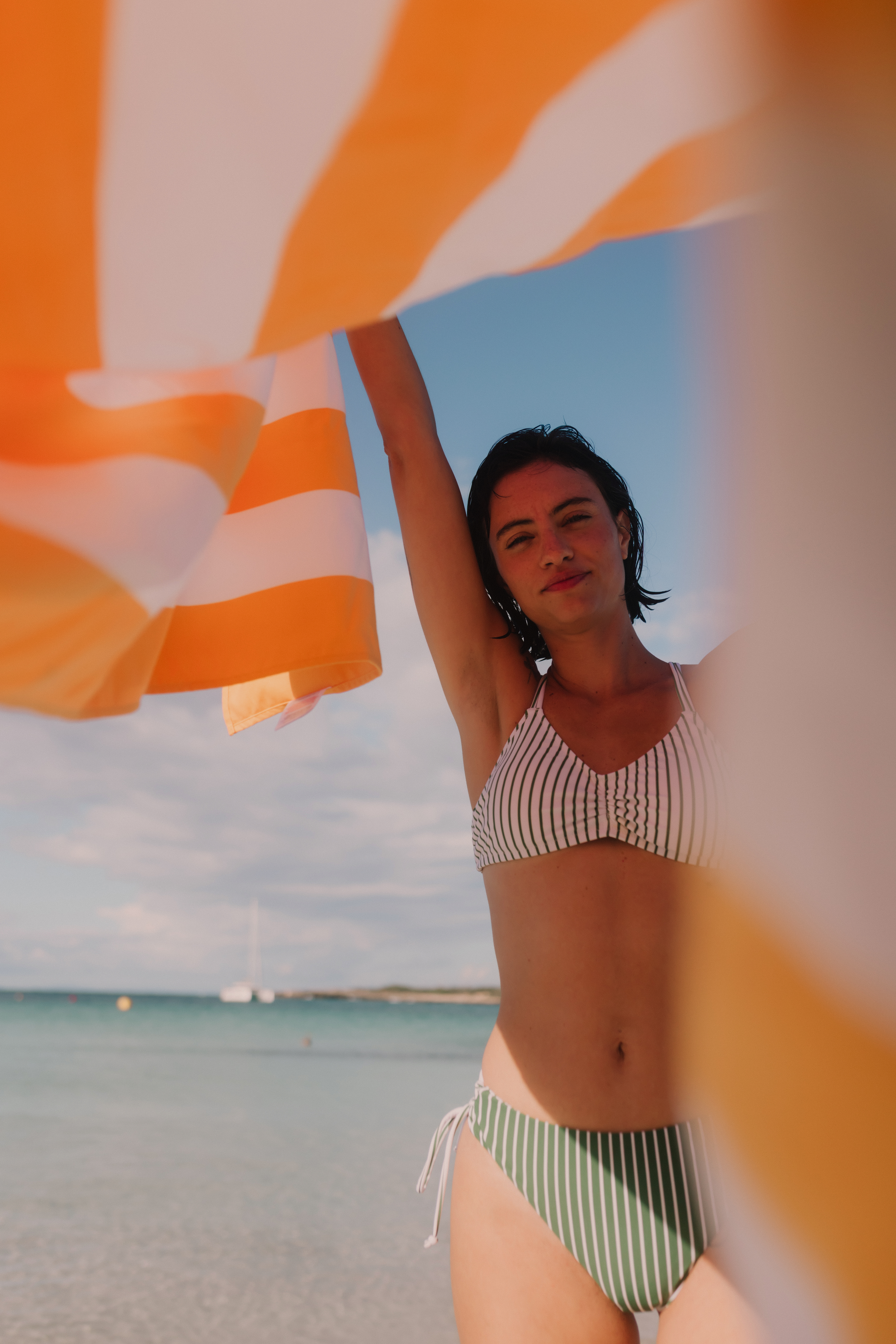 Woman in a bikini holding an orange and white striped towel at the beach.