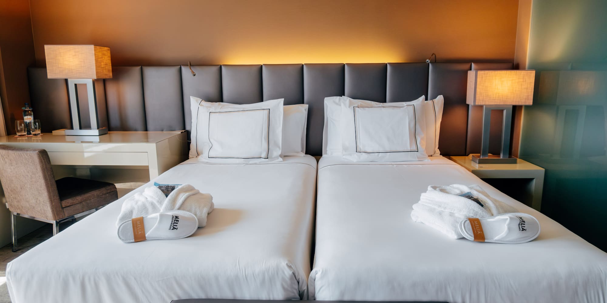 Hotel room with two twin beds, white linens, bathrobes, and lamps.