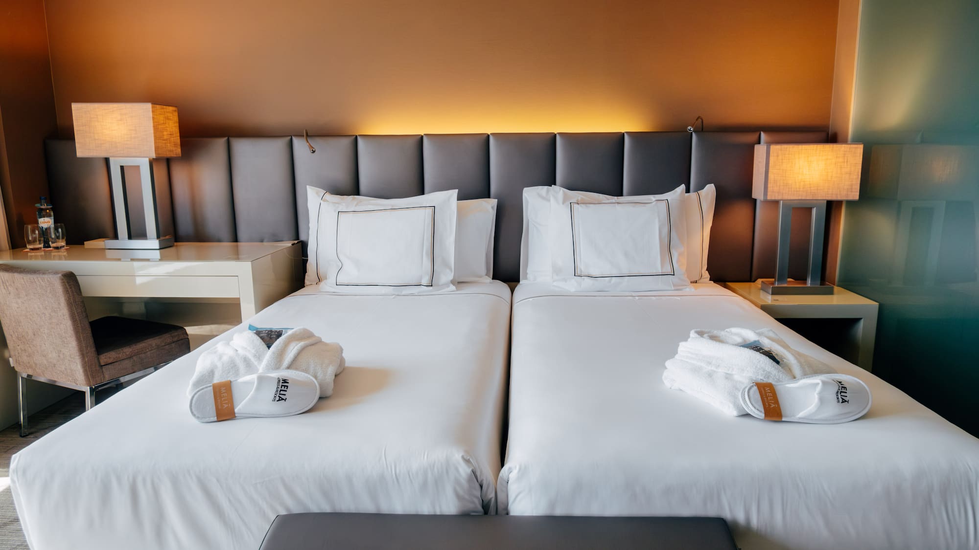 Hotel room with two twin beds, white linens, bathrobes, and lamps.