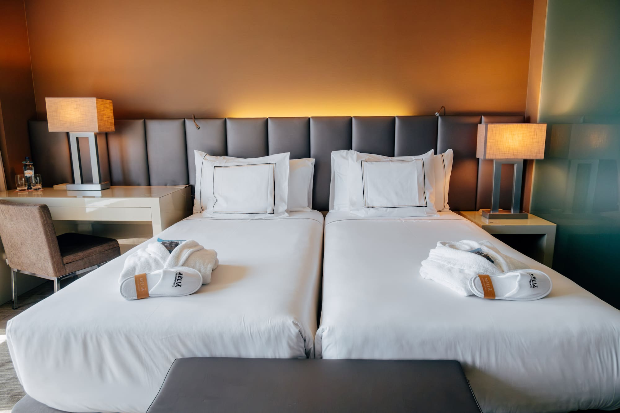 Hotel room with two twin beds, white linens, bathrobes, and lamps.