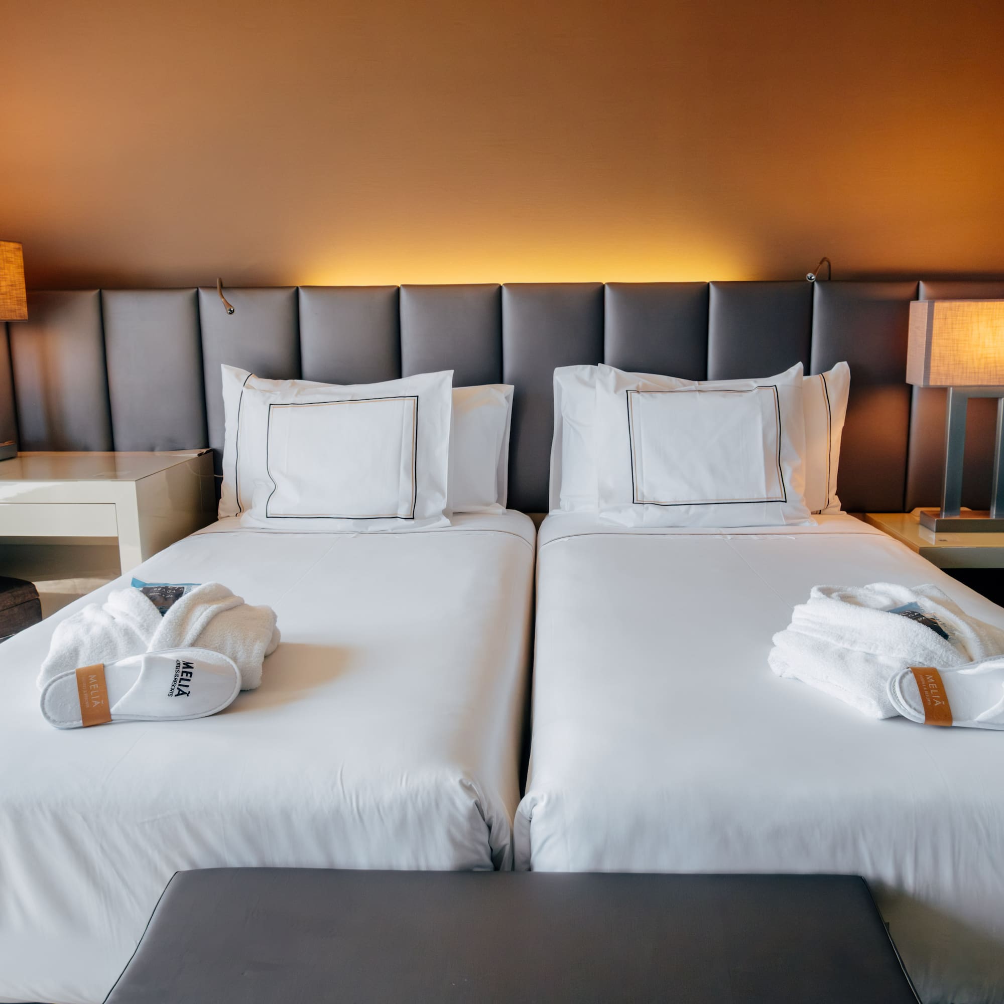 Hotel room with two twin beds, white linens, bathrobes, and lamps.