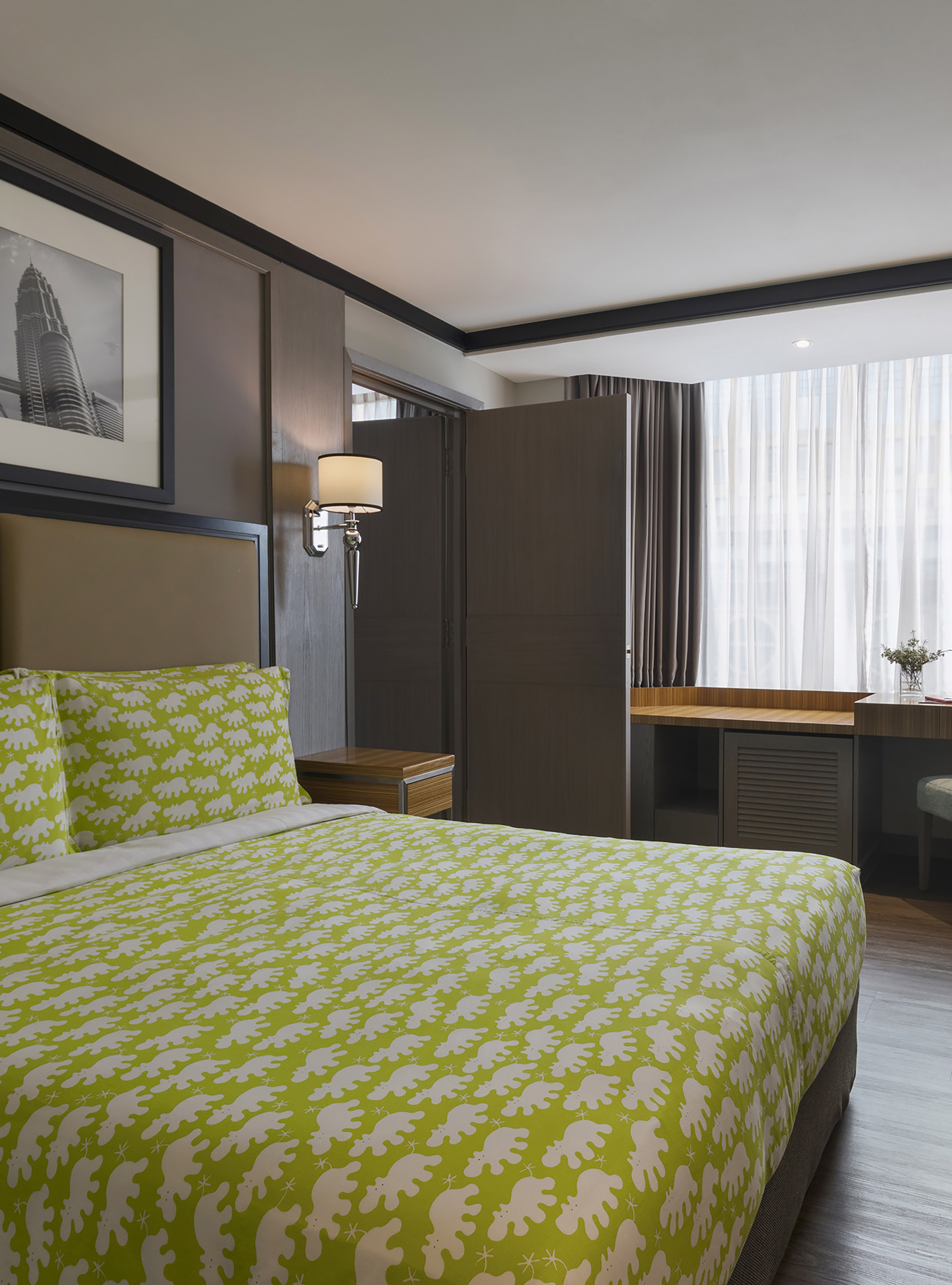 Modern hotel bedroom with vibrant green patterned bedding, desk, and large window.