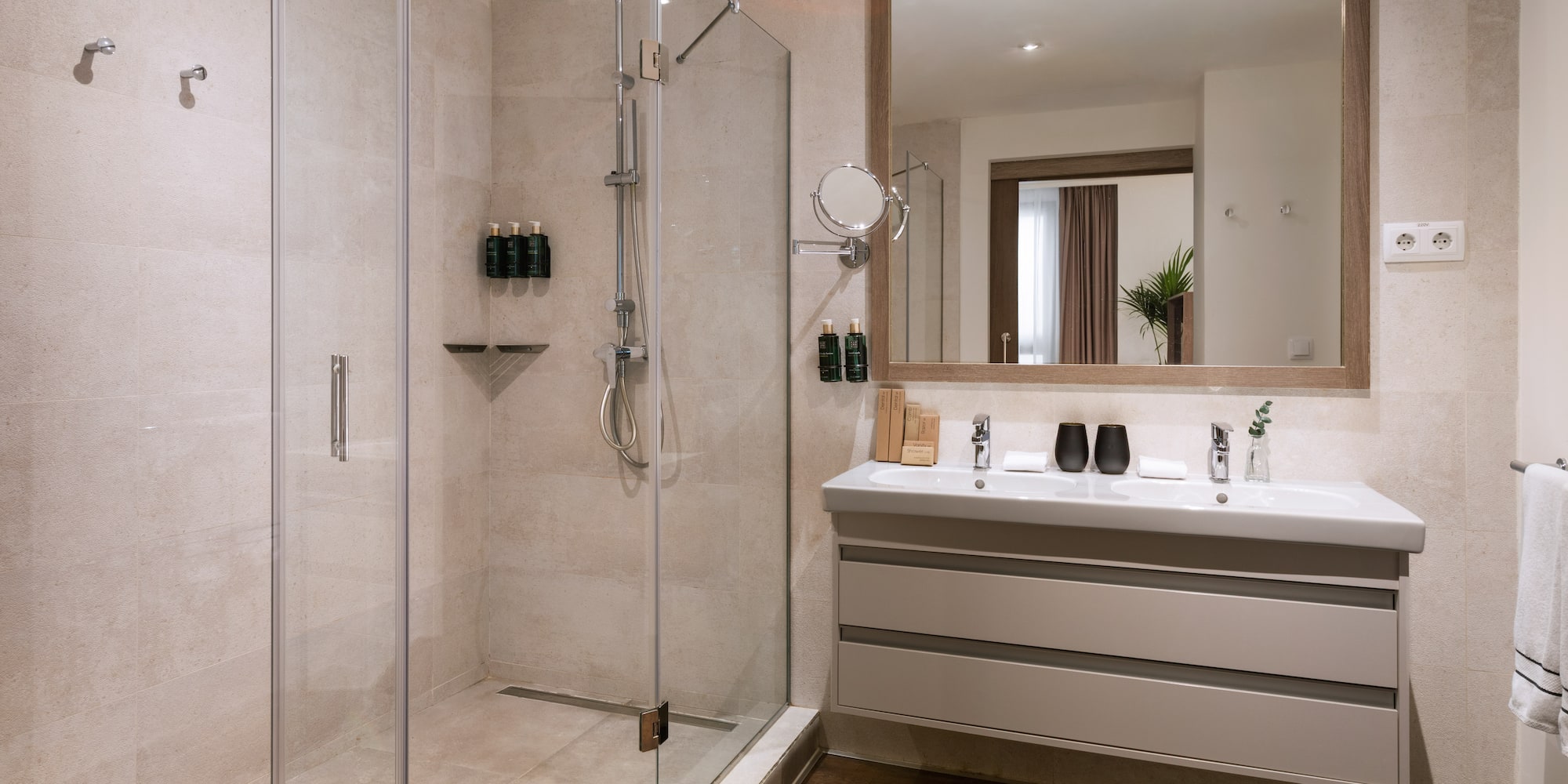 Modern hotel bathroom with glass walk-in shower and double vanity.
