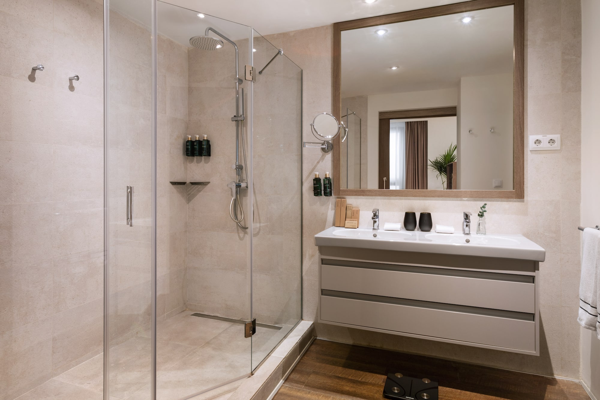 Modern hotel bathroom with glass walk-in shower and double vanity.