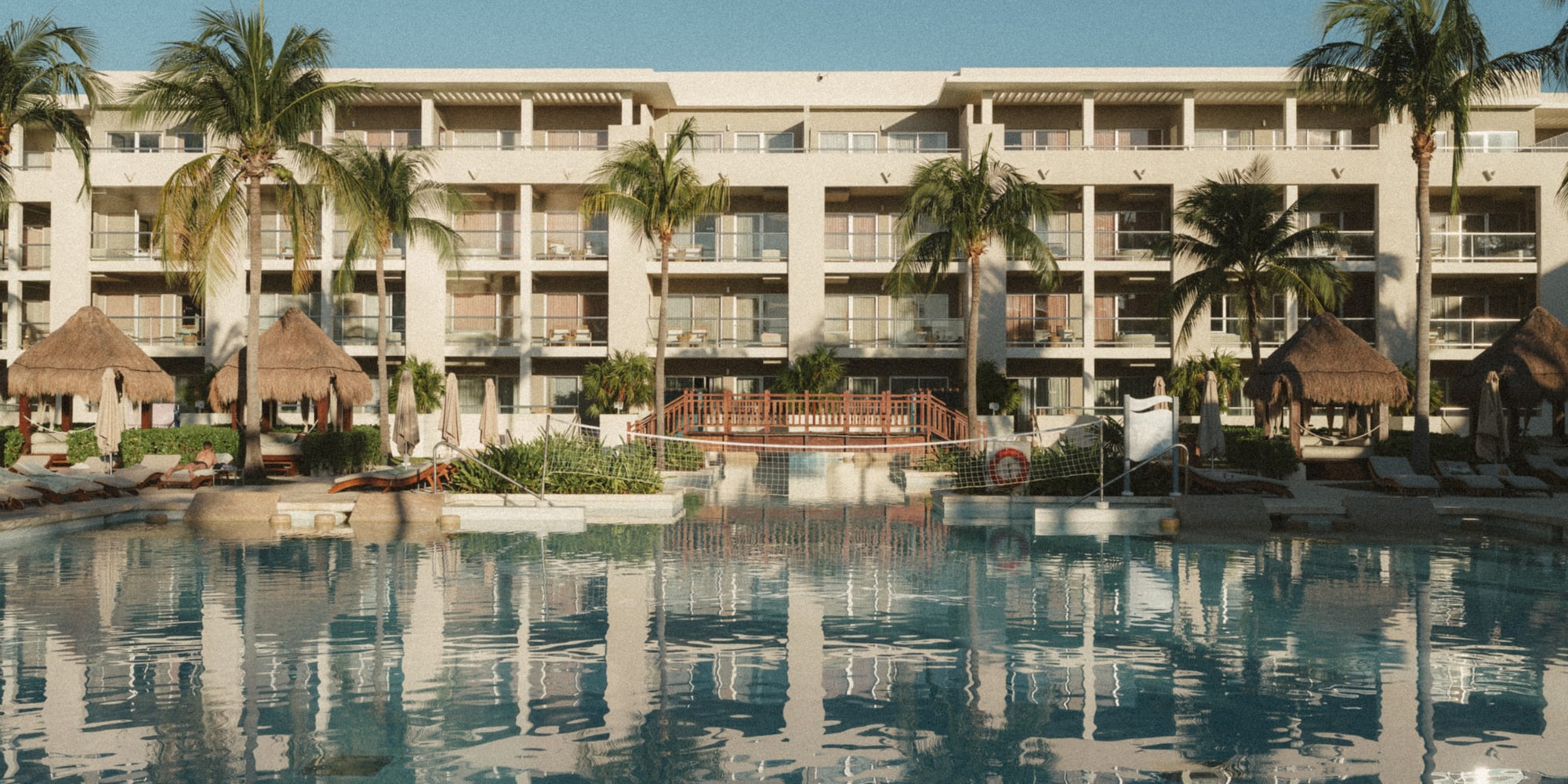 a pool with palm trees and a building with a thatched roof