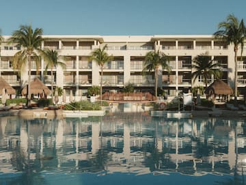 a pool with palm trees and a building with a thatched roof