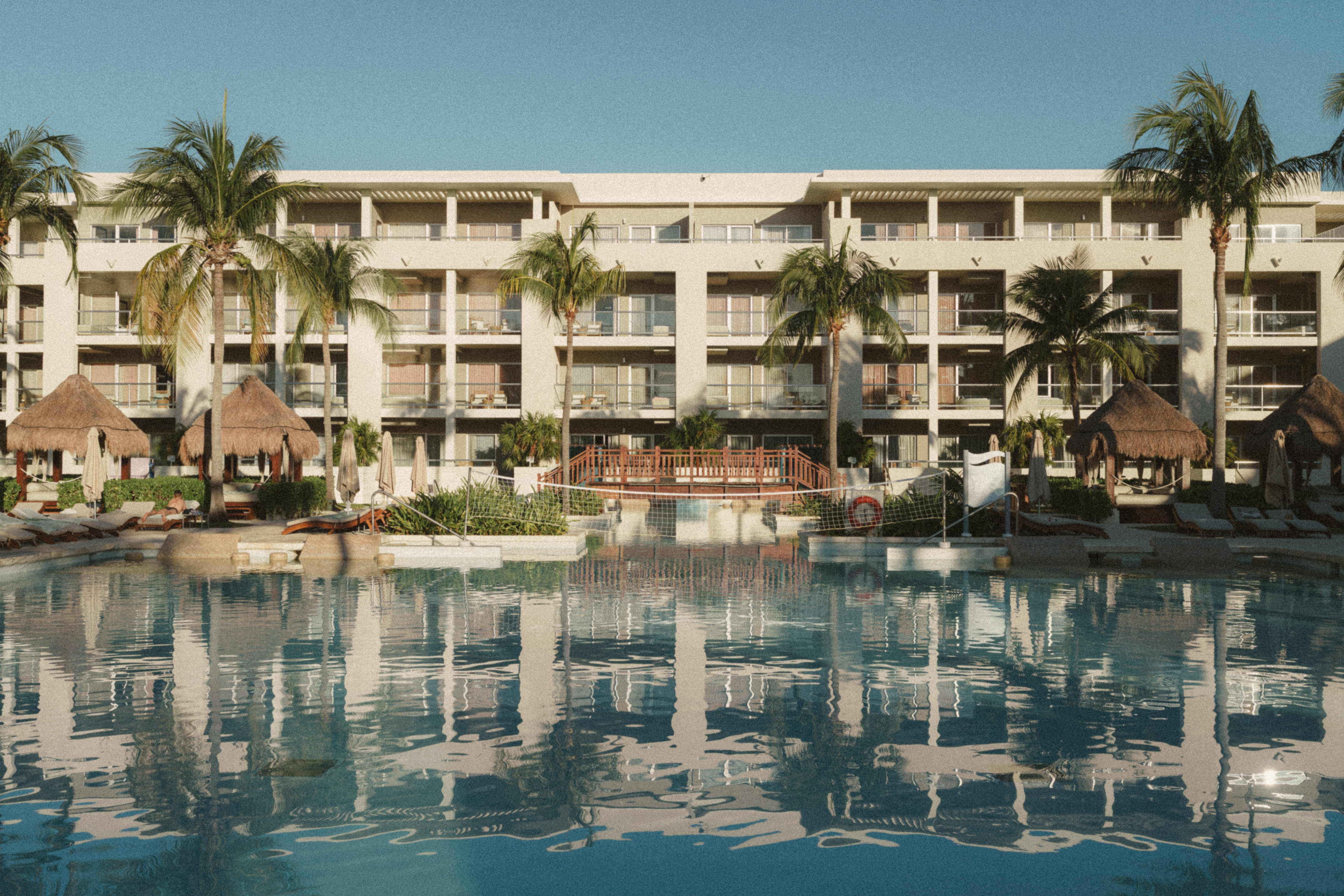 a pool with palm trees and a building with a thatched roof