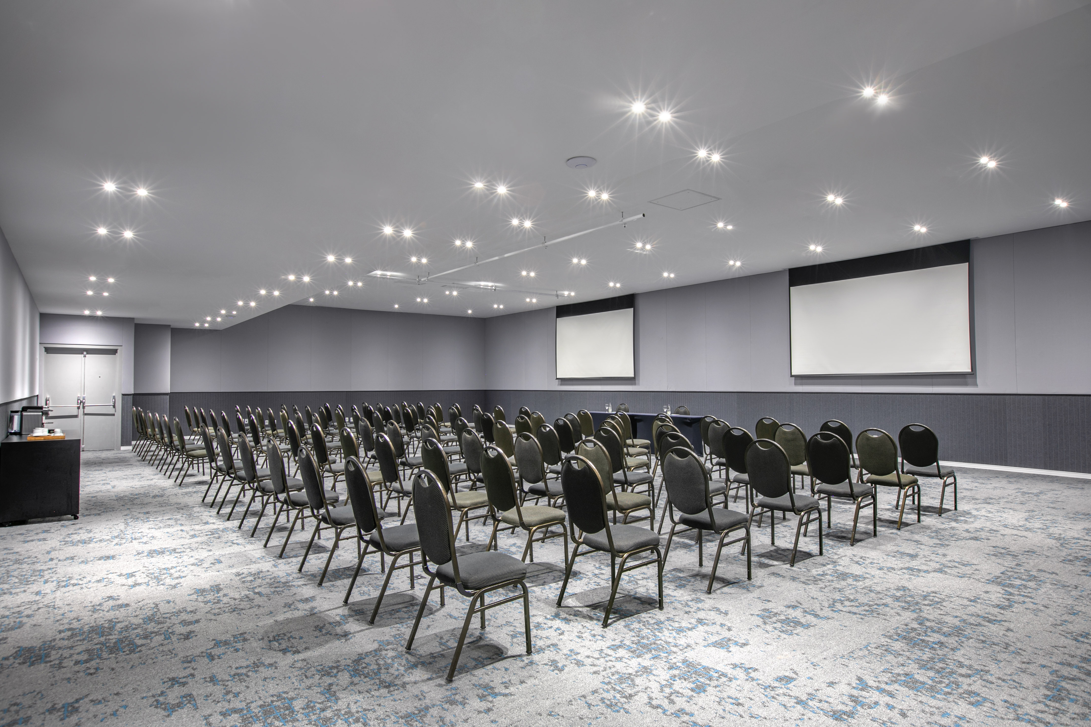 Spacious conference room with rows of chairs, twin projector screens, modern lighting.