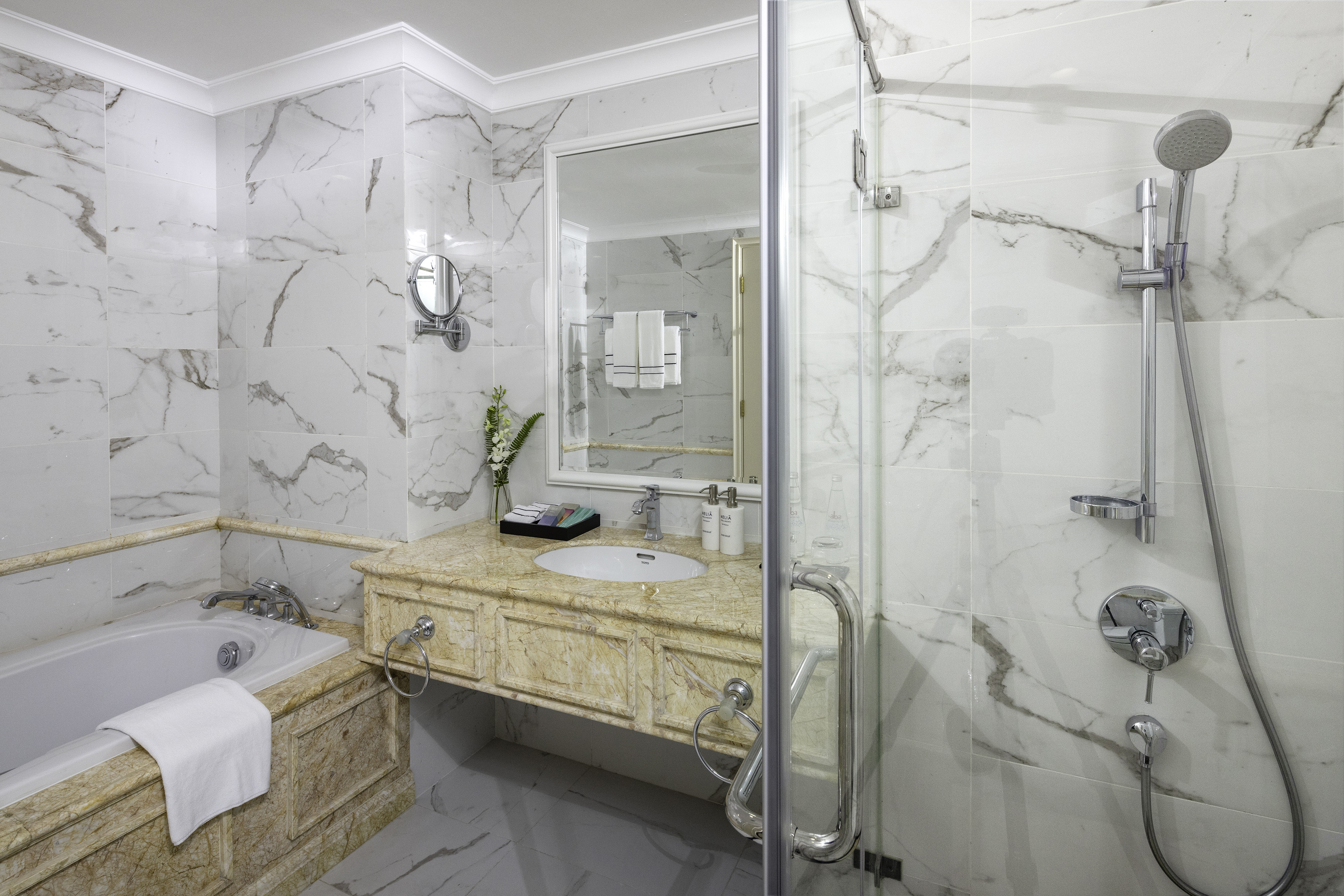 Elegant white marble hotel bathroom featuring a tub, vanity, and shower.