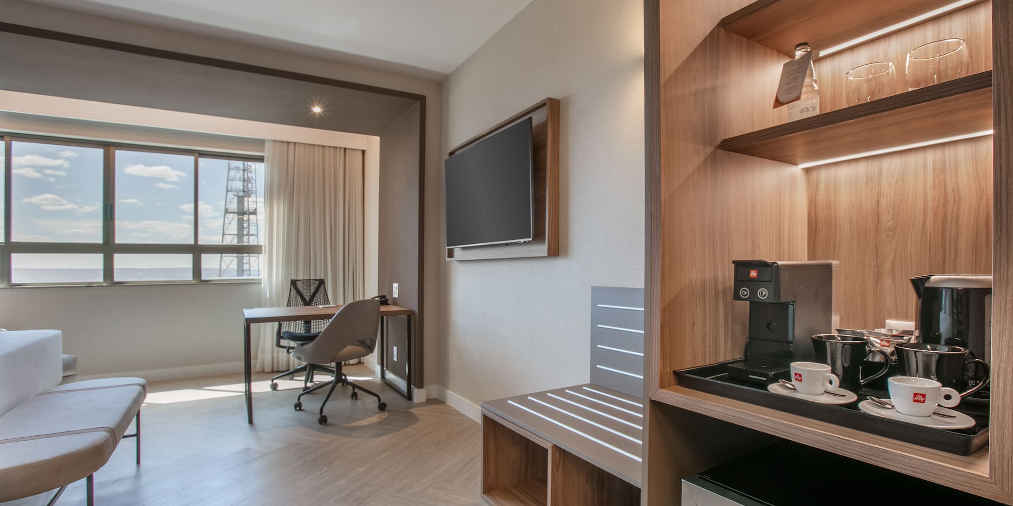 Spacious hotel room with work desk, city view, TV, and coffee minibar.
