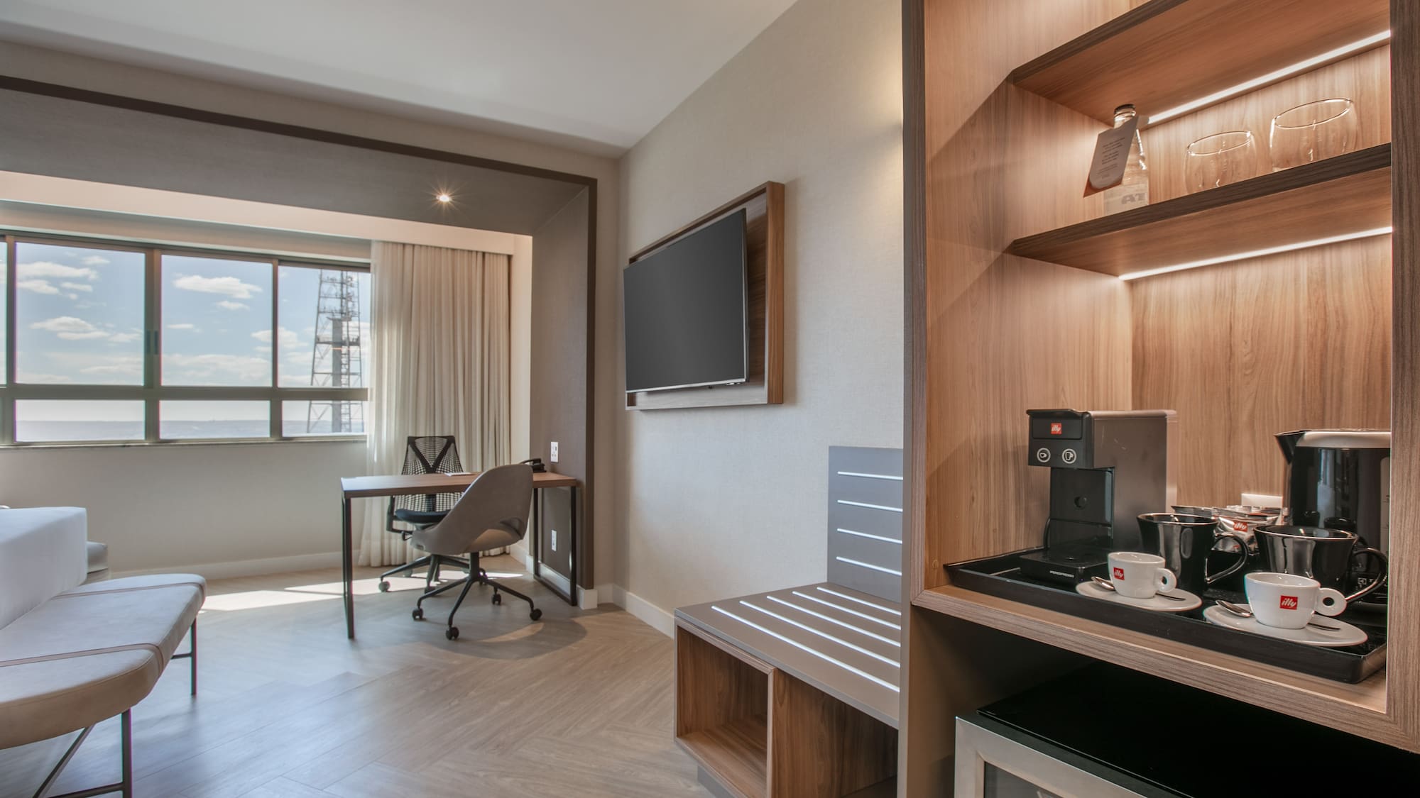 Spacious hotel room with work desk, city view, TV, and coffee minibar.