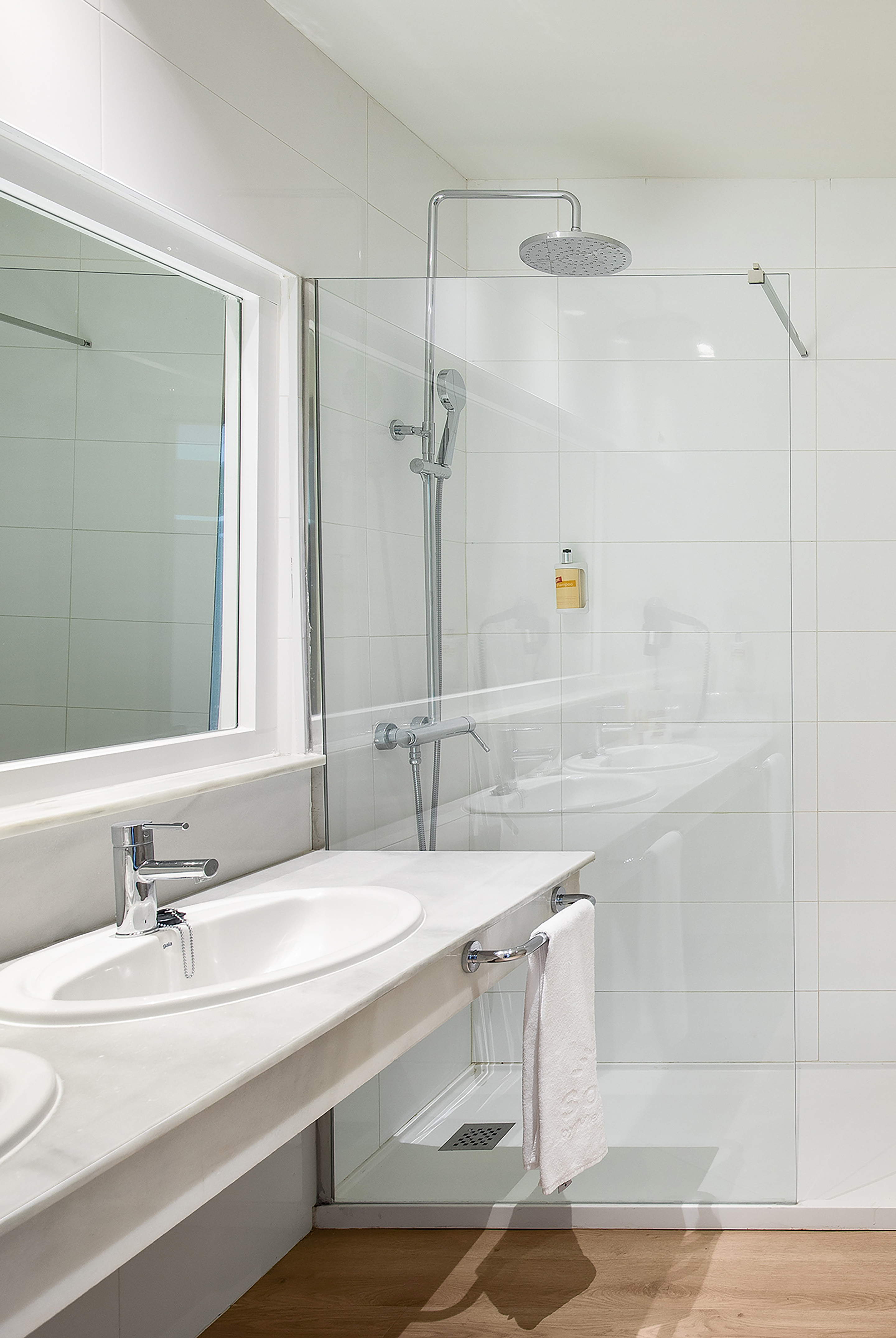 Modern hotel bathroom with white vanity, sink, and glass shower.