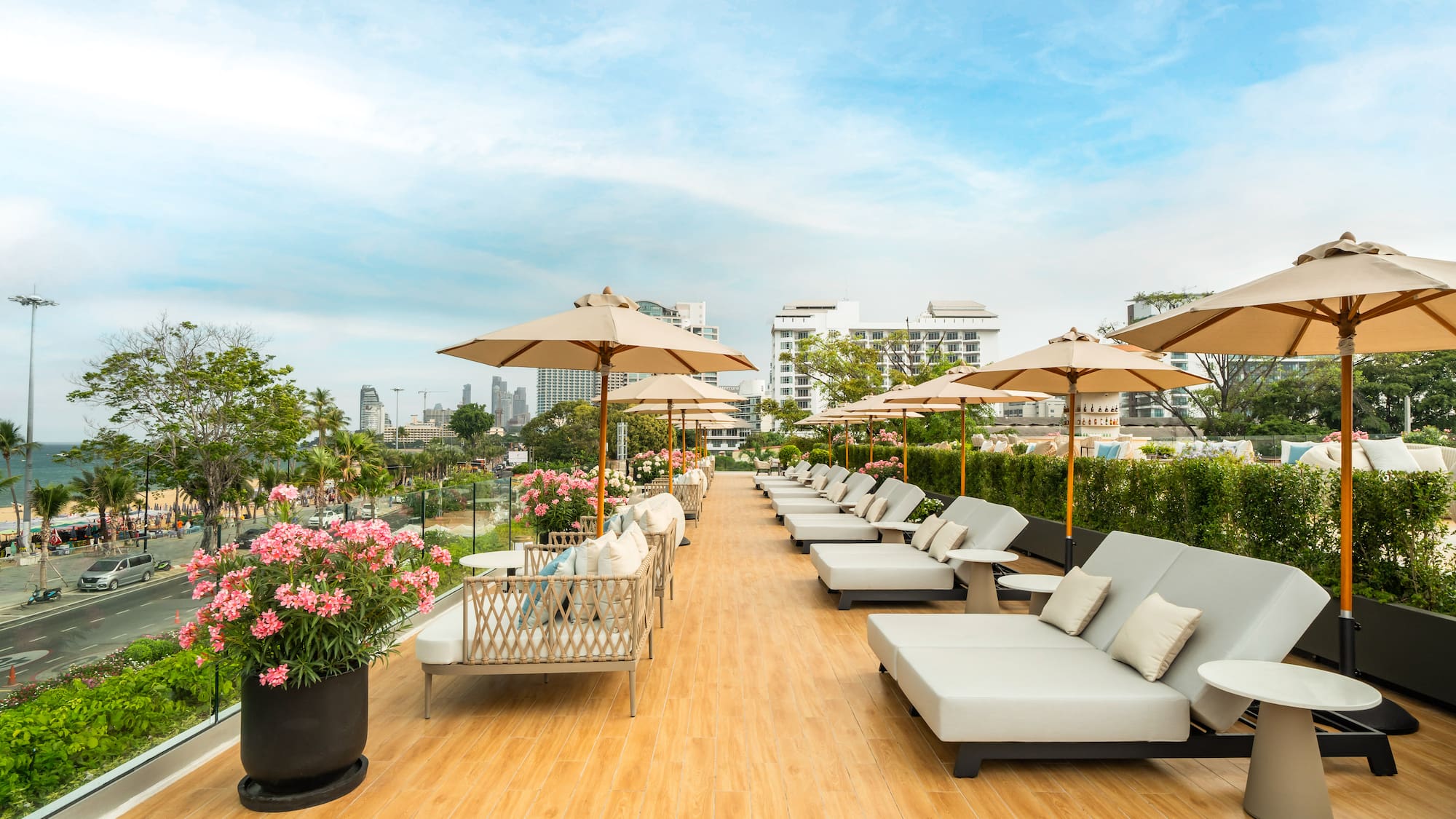 Rooftop terrace with sun loungers, umbrellas, and Pattaya city beach skyline view.