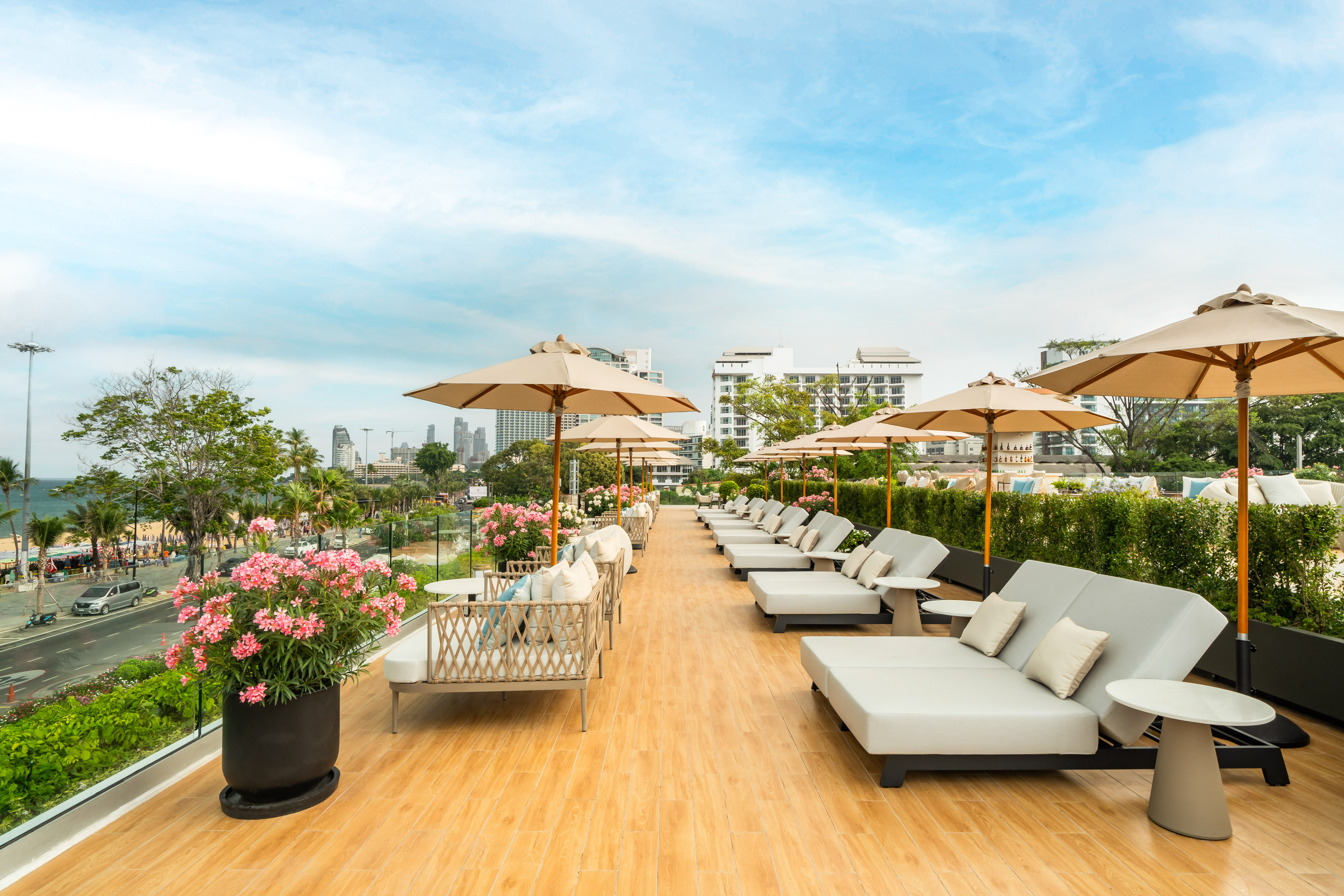 Rooftop terrace with sun loungers, umbrellas, and Pattaya city beach skyline view.