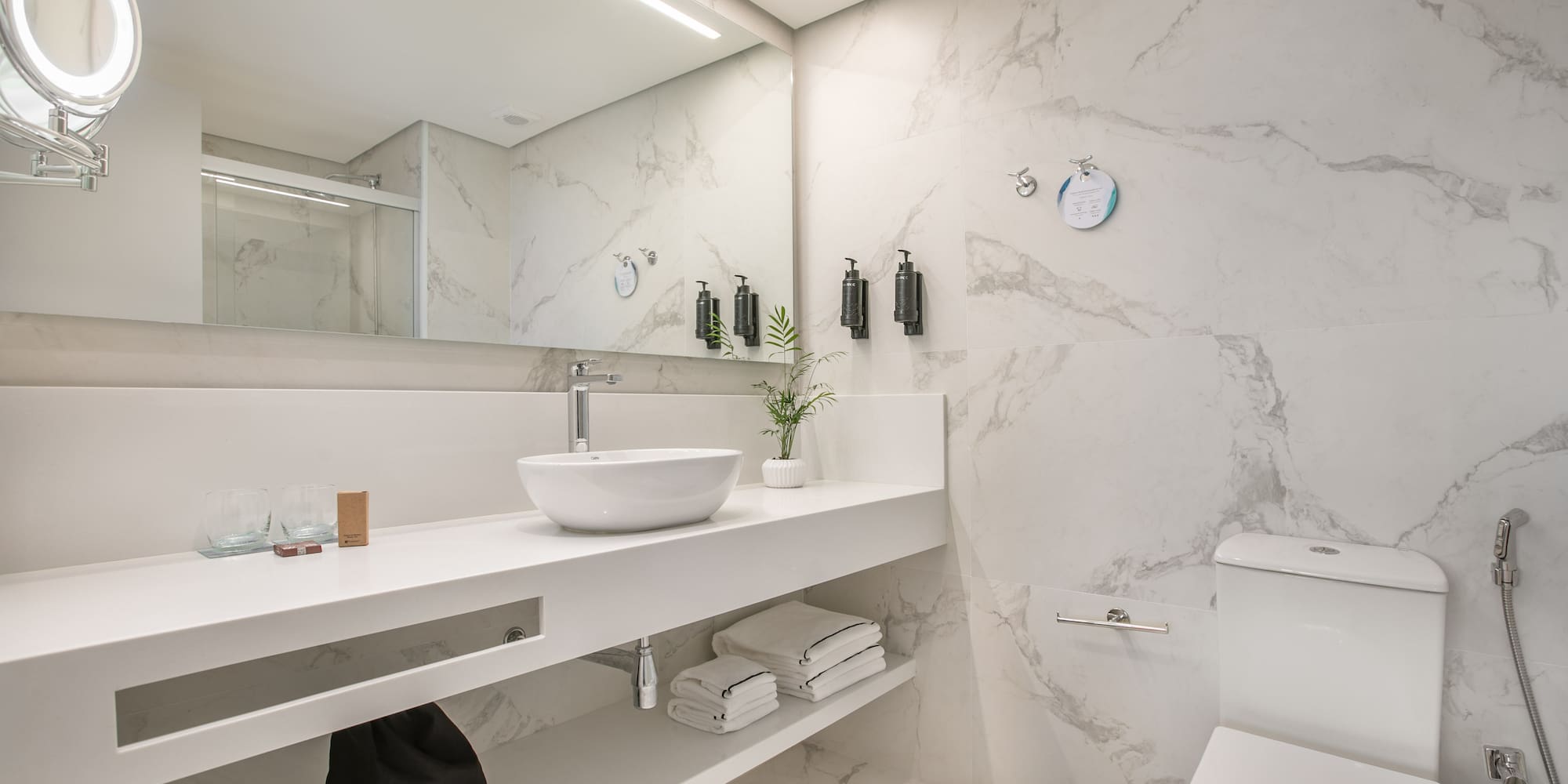 Modern white marble bathroom with vanity, vessel sink, toilet, and shower.