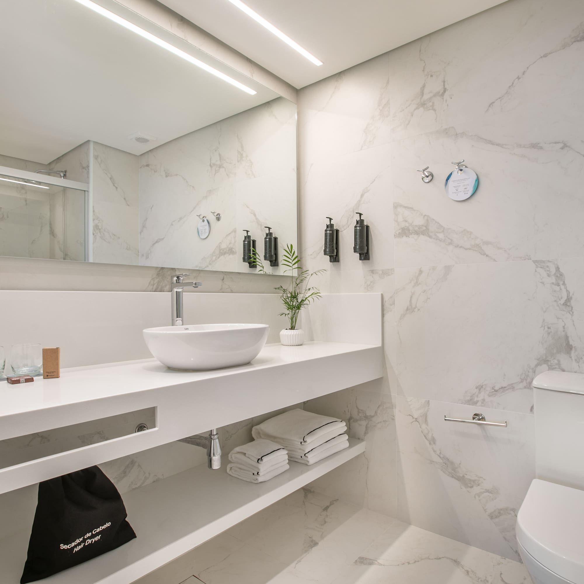 Modern white marble bathroom with vanity, vessel sink, toilet, and shower.