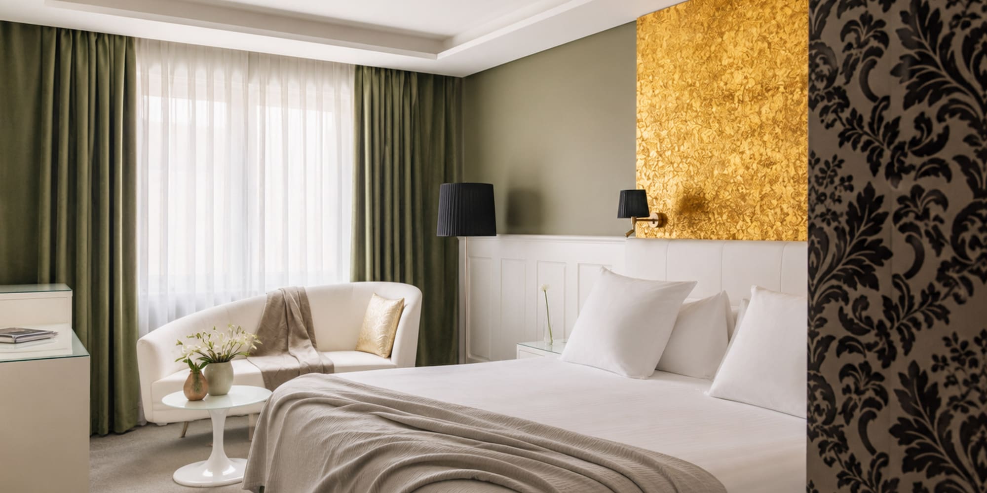 Luxury hotel room with gold accent wall, white bed, olive green curtains.