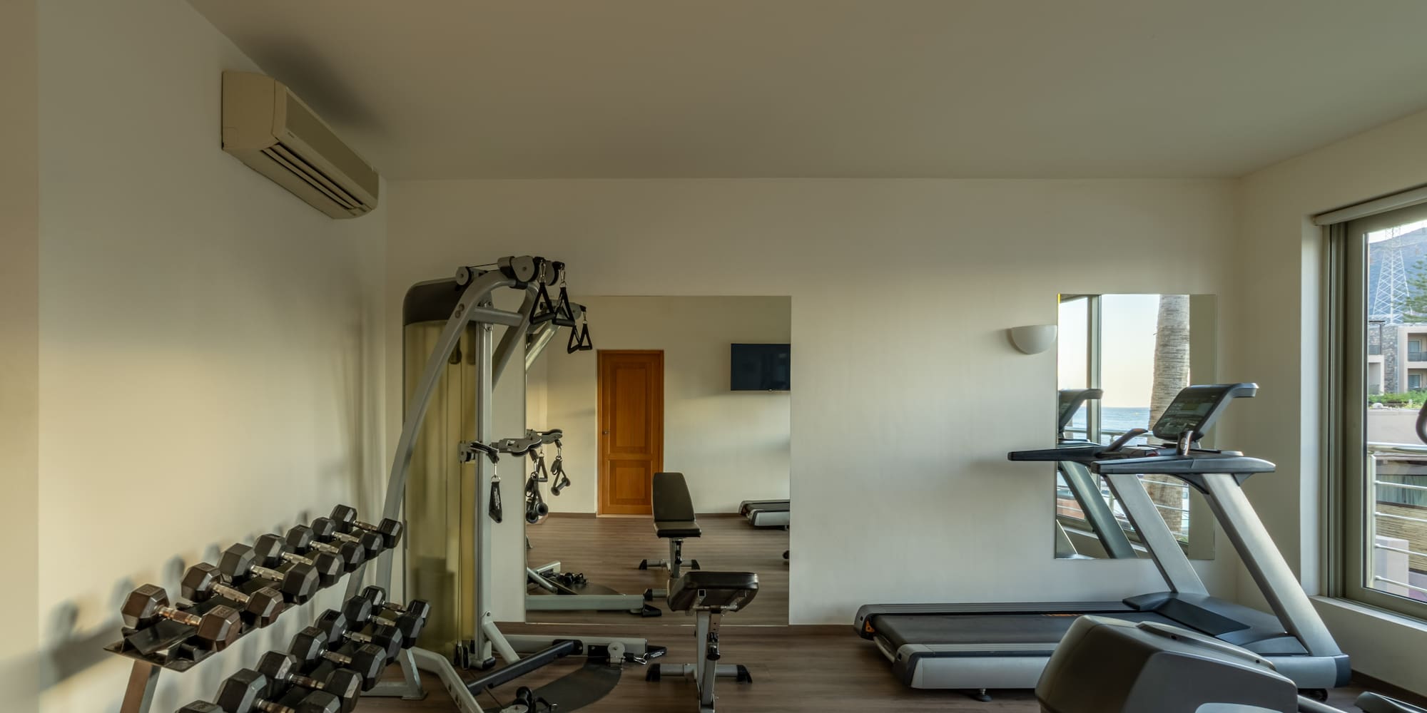 Fitness room with dumbbells, multi-station, treadmill, and ocean view.